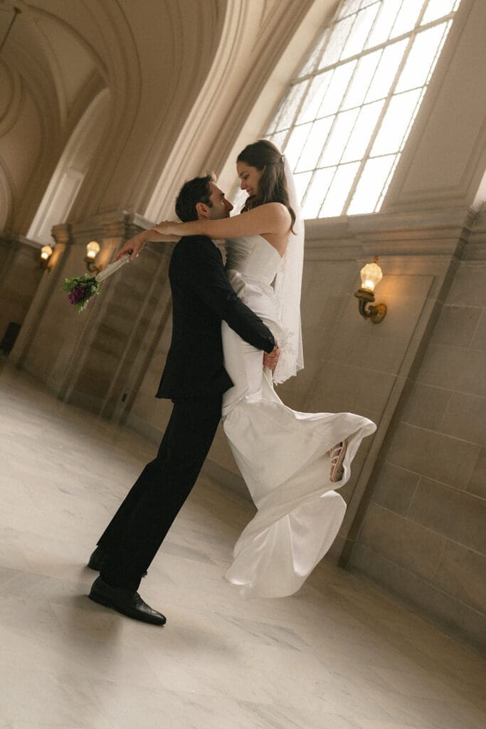 Groom lifting up bride and swinging her around in San Francisco City Hall