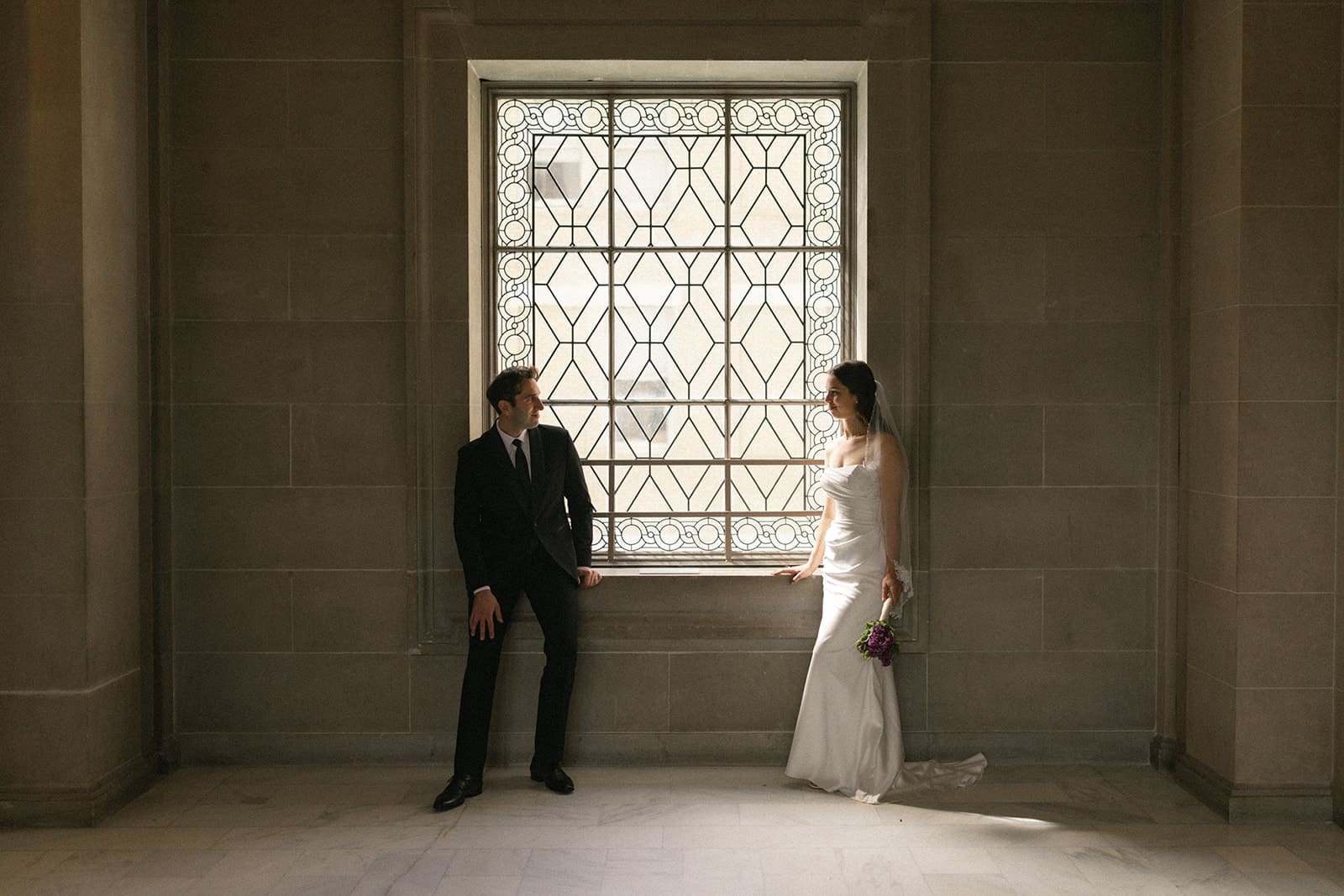 Bride and groom portrait inside San Francisco City Hall next to iconic windows