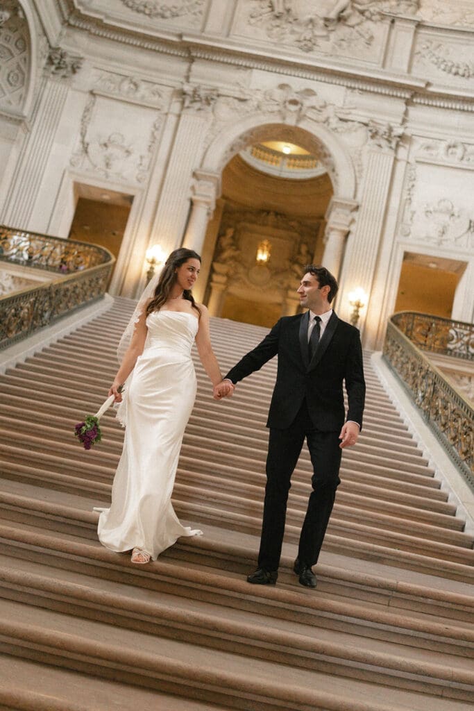Bride and groom portrait inside San Francisco City Hall walking down grand staircase