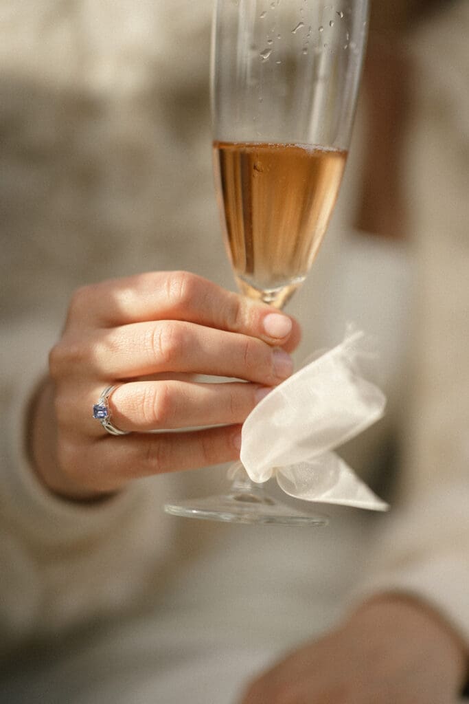 Bride holding glass of champagne during cocktail hour and showcasing ring