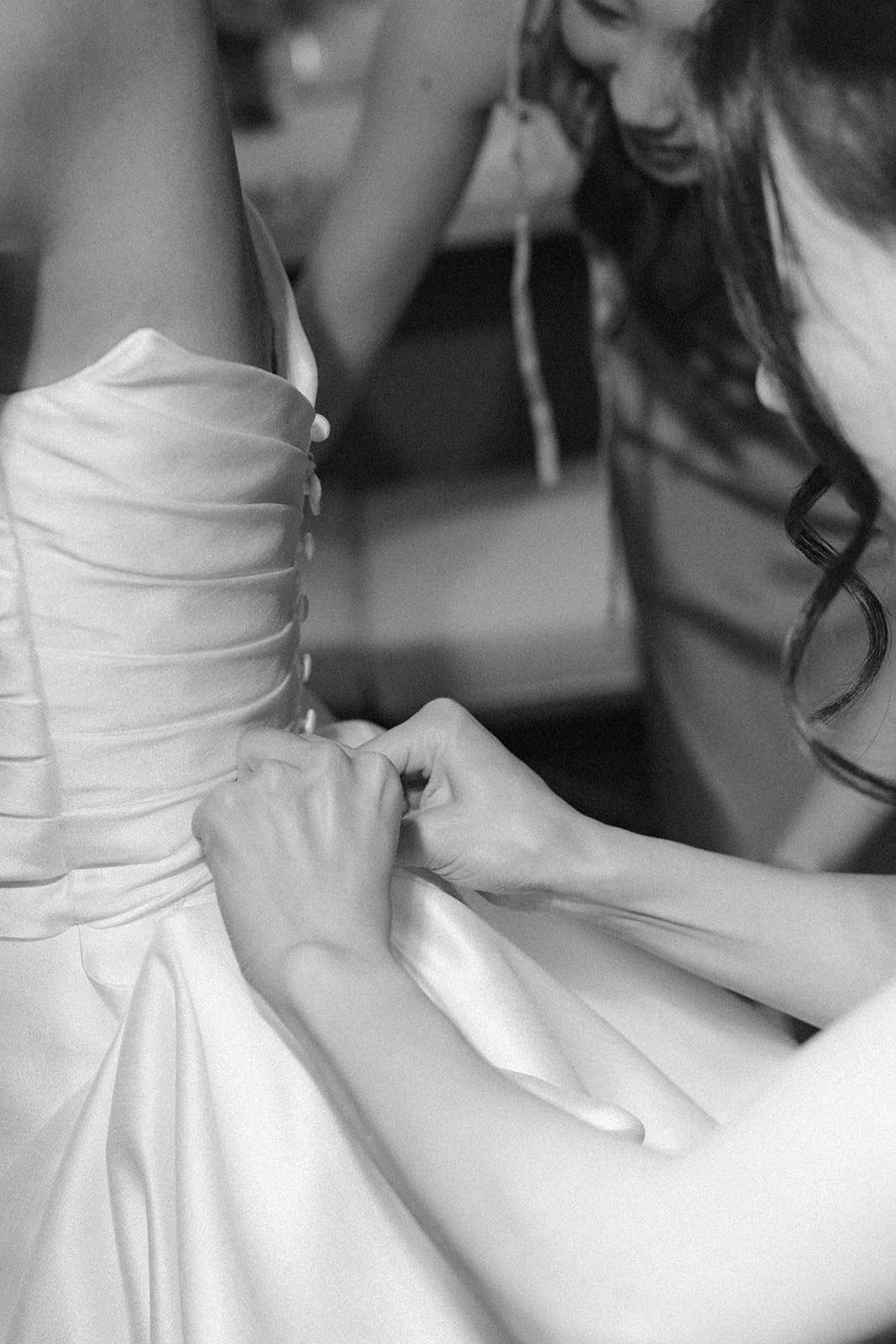 Bridesmaid fastening the back of the bride's satin wedding dress before the ceremony at casa real at ruby hill winery, one of the premier bay area wedding venues.