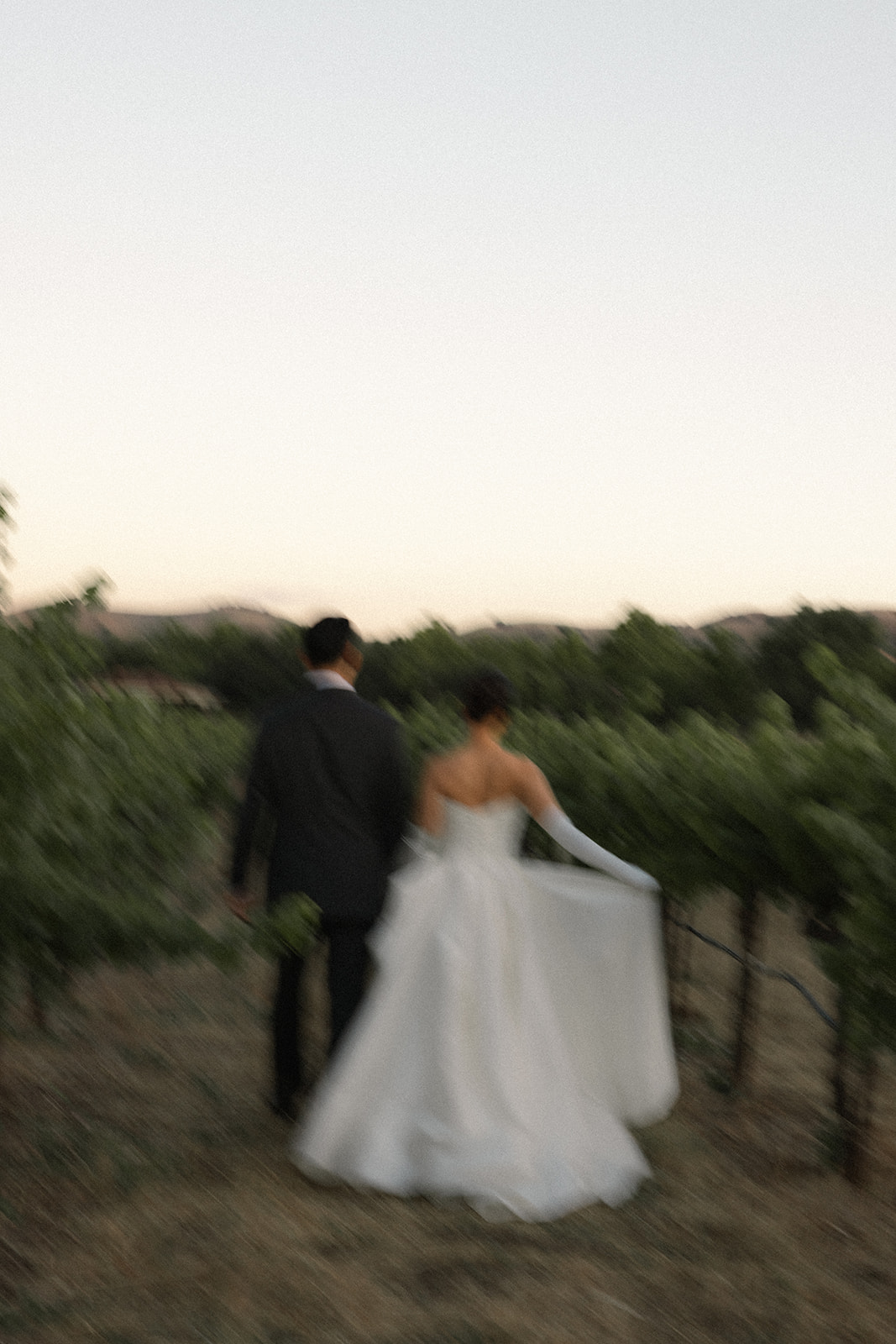 Bride and groom walk hand in hand through the vineyard with artistic motion blur at casa real at ruby hill winery, featured in elegant casa real at ruby hill winery photos.