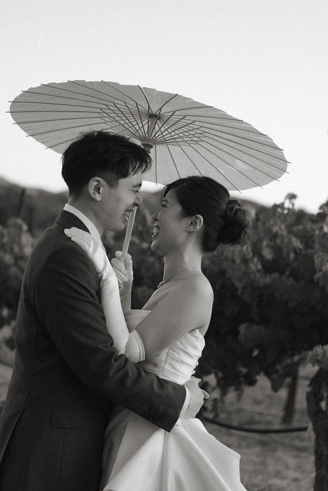 Bride and groom embracing beneath a white parasol in the vineyard at casa real at ruby hill winery, photographed by a bay area wedding photographer.