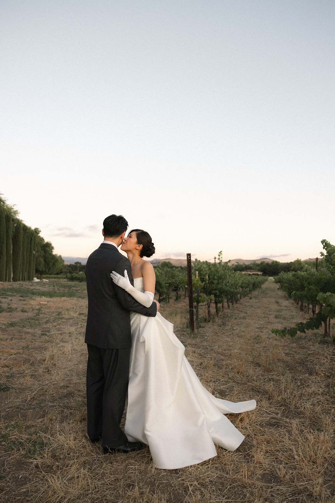 Bride kisses the groom while embracing in the vineyard during golden hour at casa real at ruby hill winery, showcasing romantic casa real at ruby hill winery photos.