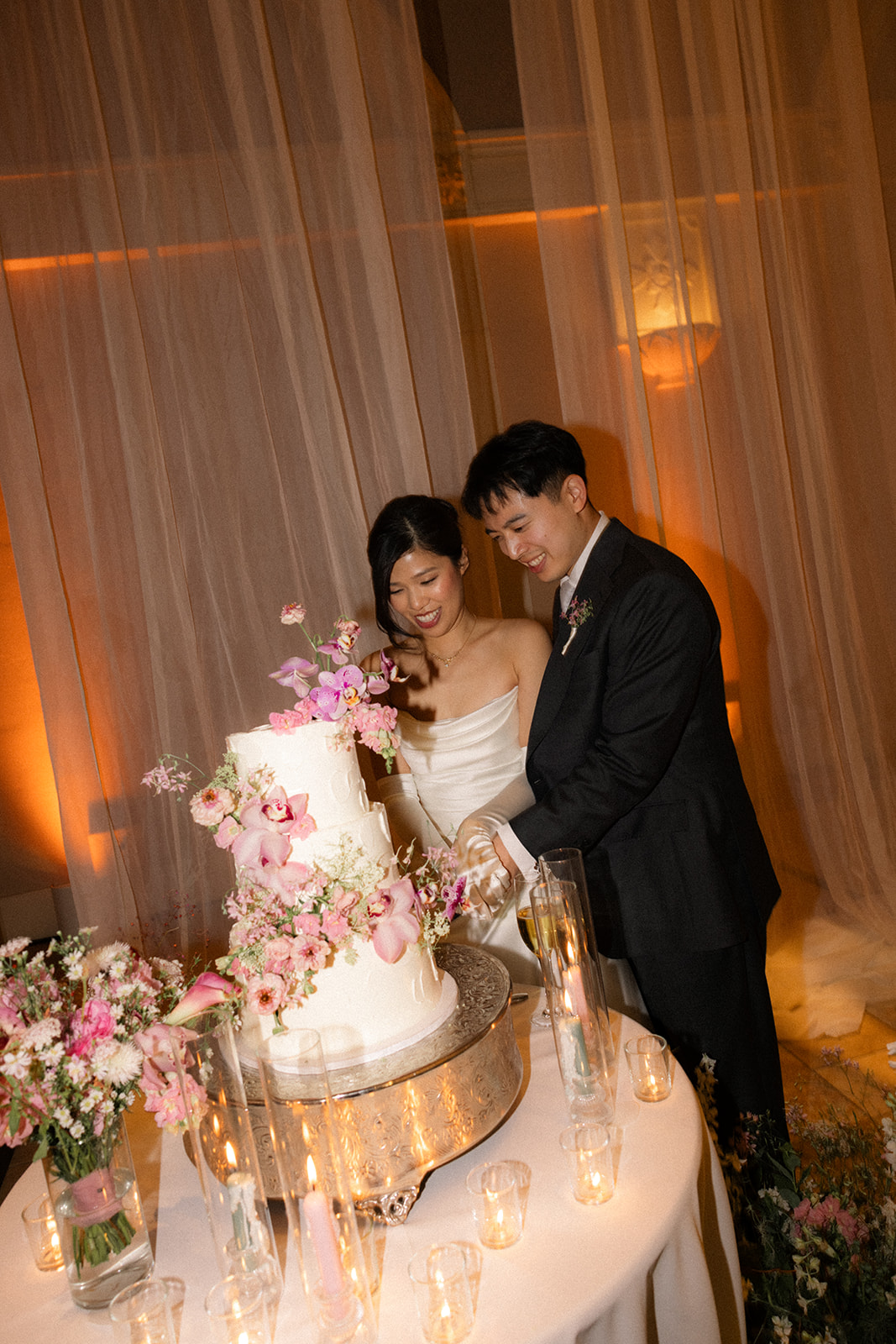 Bride and groom cut a three-tier floral wedding cake surrounded by candles and pink blooms at casa real at ruby hill winery, featured in casa real at ruby hill winery photos.