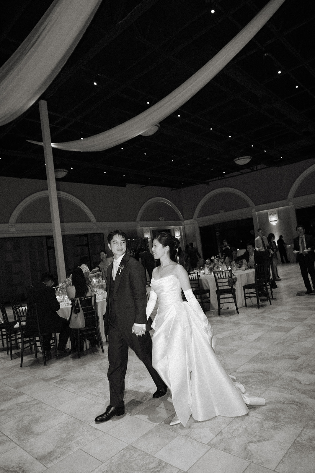 Bride and groom hold hands as they walk across the reception space beneath flowing drapery at casa real at ruby hill winery, featured in casa real at ruby hill winery photos.