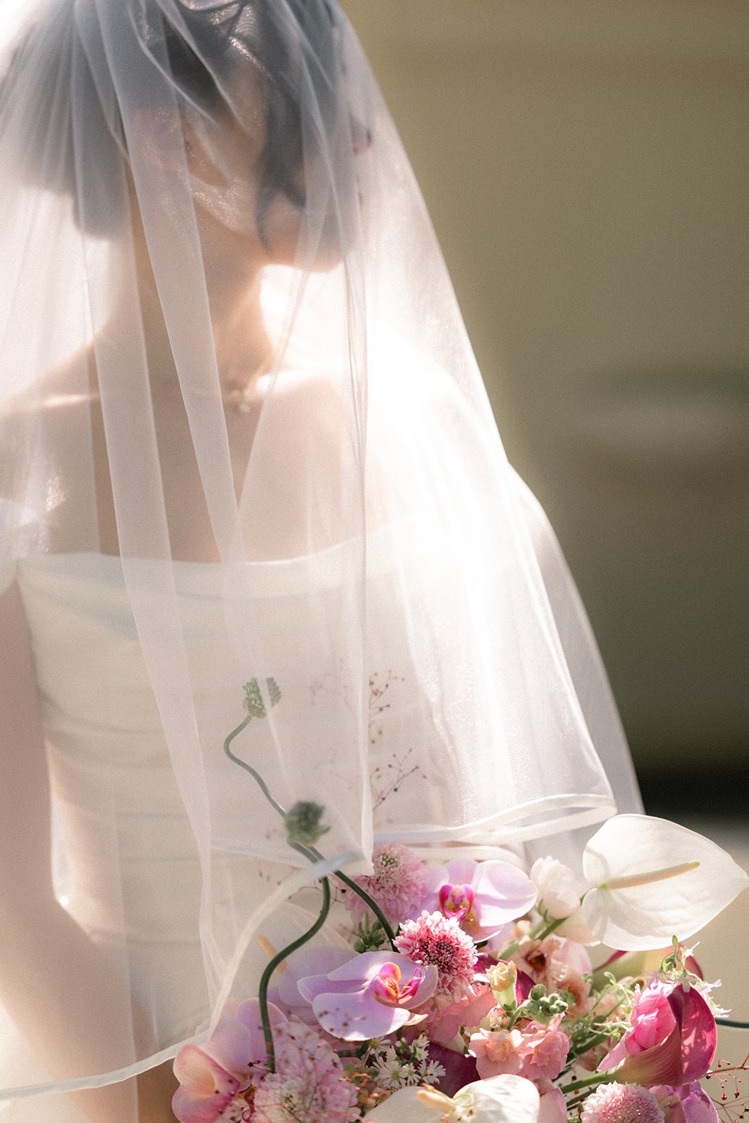 Soft portrait of the bride behind her veil holding a pink and white floral bouquet during portraits at casa real at ruby hill winery, photographed by a bay area wedding photographer.