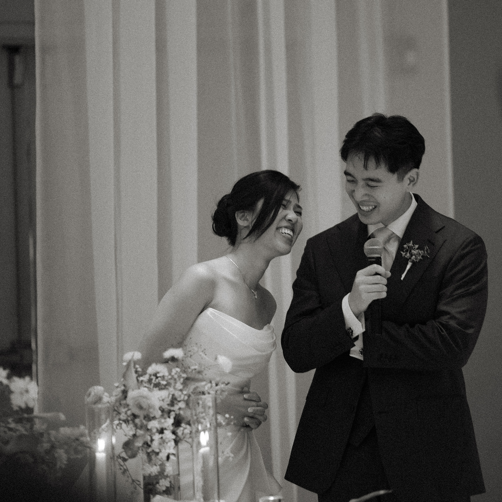 Bride and groom laugh together while giving a heartfelt wedding speech with a microphone, captured in timeless casa real at ruby hill winery photos.