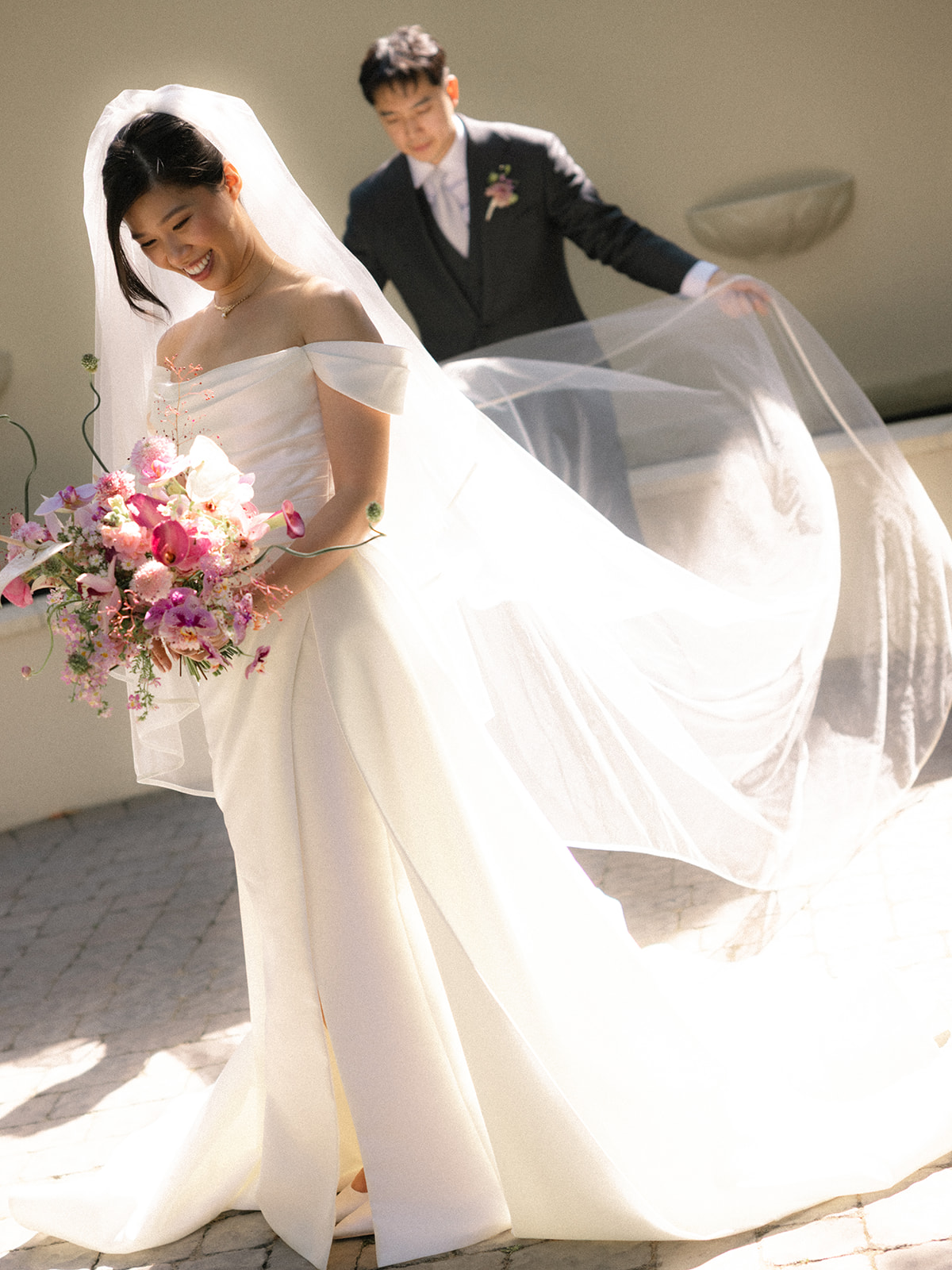 Bride holding a vibrant bouquet while the groom lifts her veil during portraits at casa real at ruby hill winery.