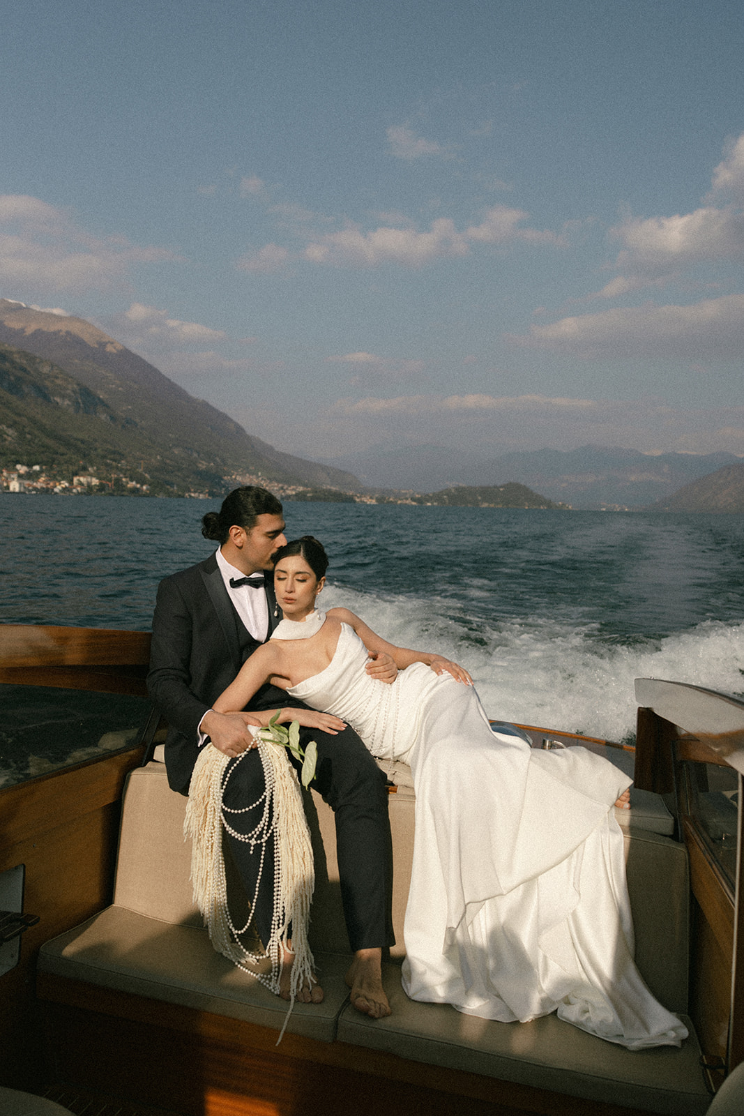 Bride and groom embracing on a vintage wooden boat as it cruises across the lake during an Italian destination wedding.