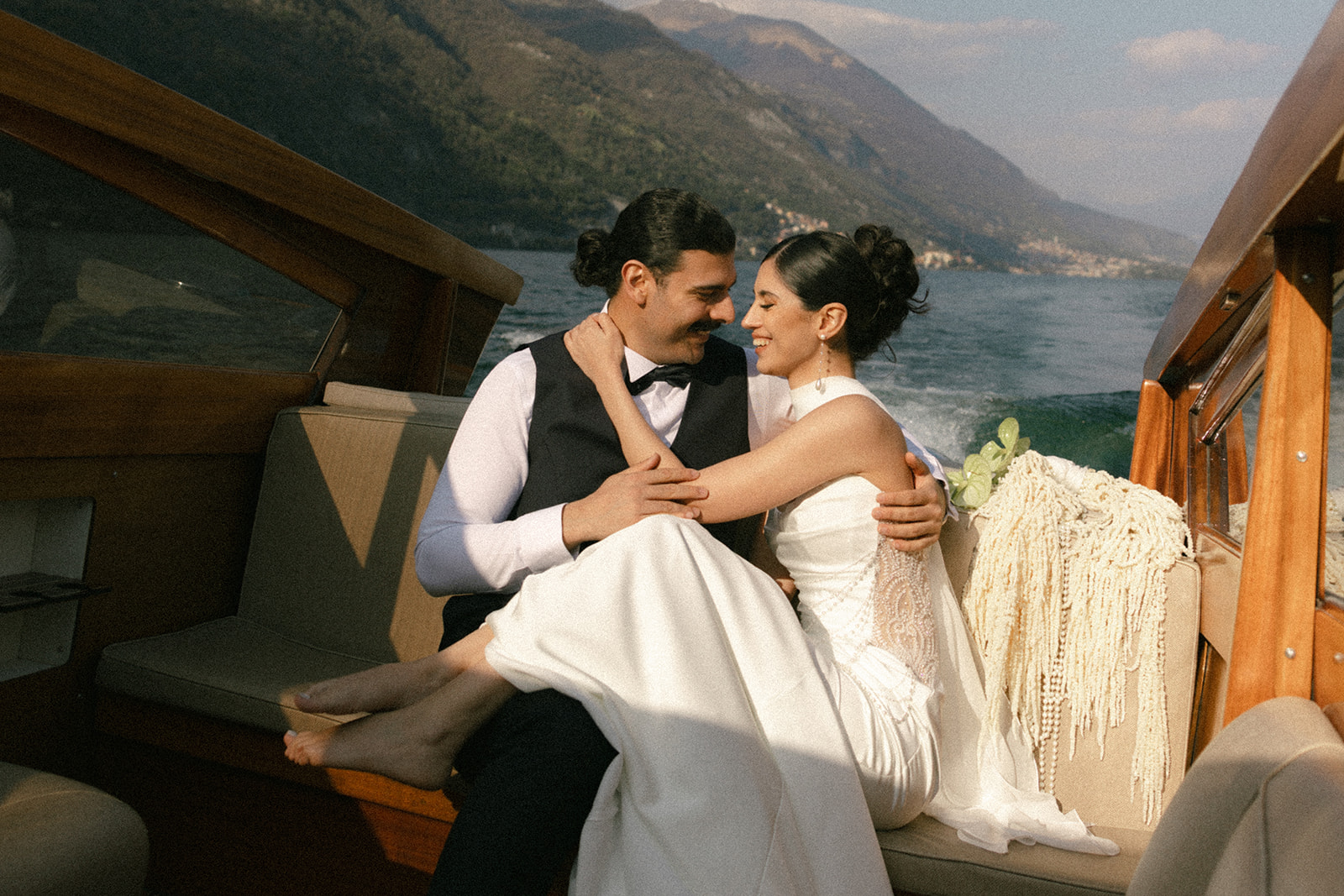 Bride and groom embracing aboard a classic wooden boat with mountain views, captured by a destination wedding photographer.