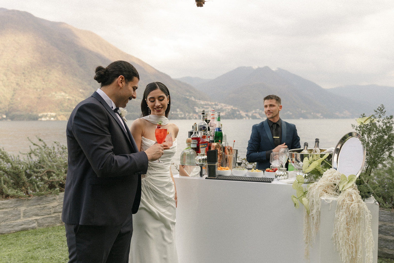 Bride and groom enjoying cocktails at an outdoor bar with Lake Como and mountain views during a Lake Como wedding.