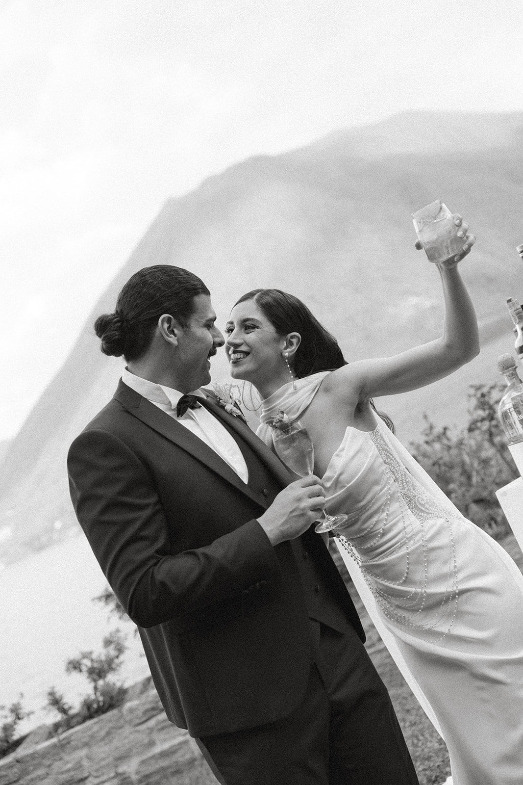 Bride raising a cocktail while smiling at the groom during a lively black-and-white moment at an Italian destination wedding.
