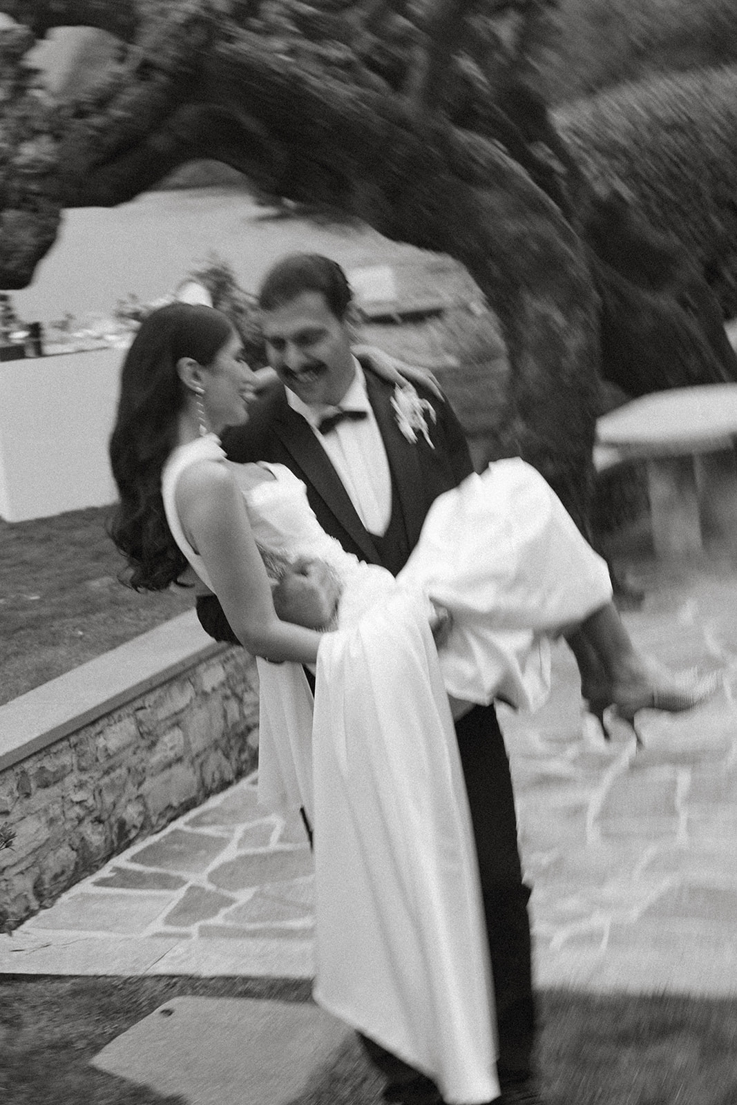 Groom carrying the bride through a garden path, captured in a candid black-and-white portrait by a destination wedding photographer.