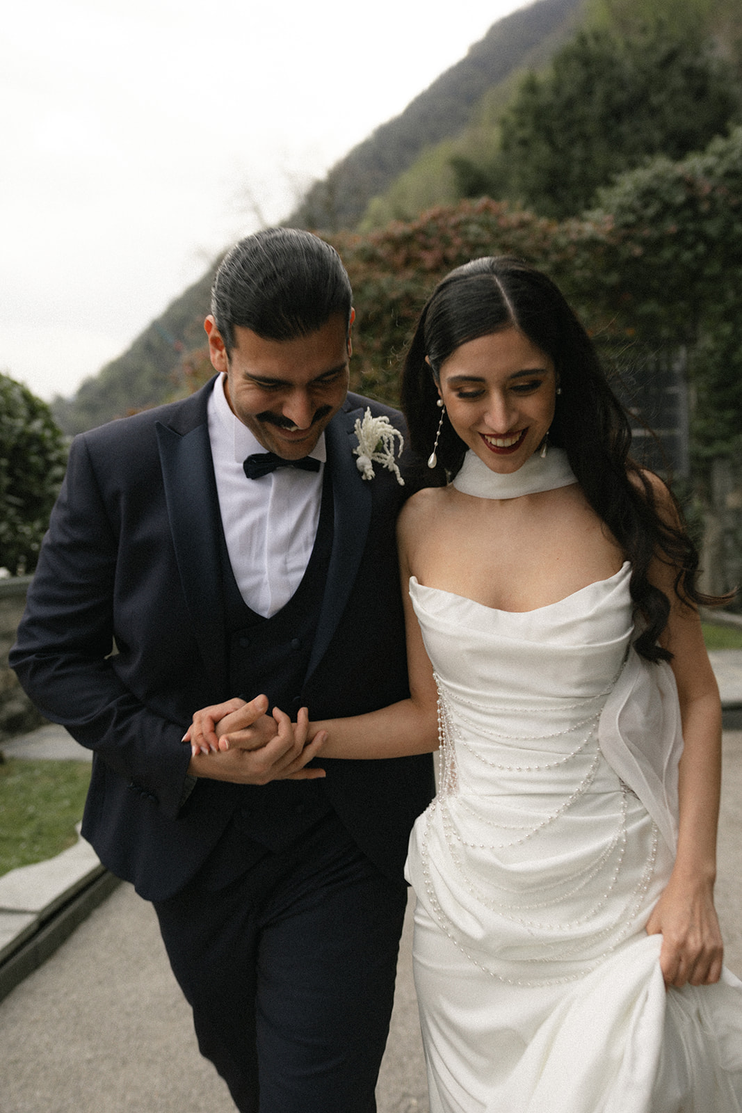 Bride and groom walking hand in hand through the garden, smiling as they share a candid moment during their wedding portrait session.