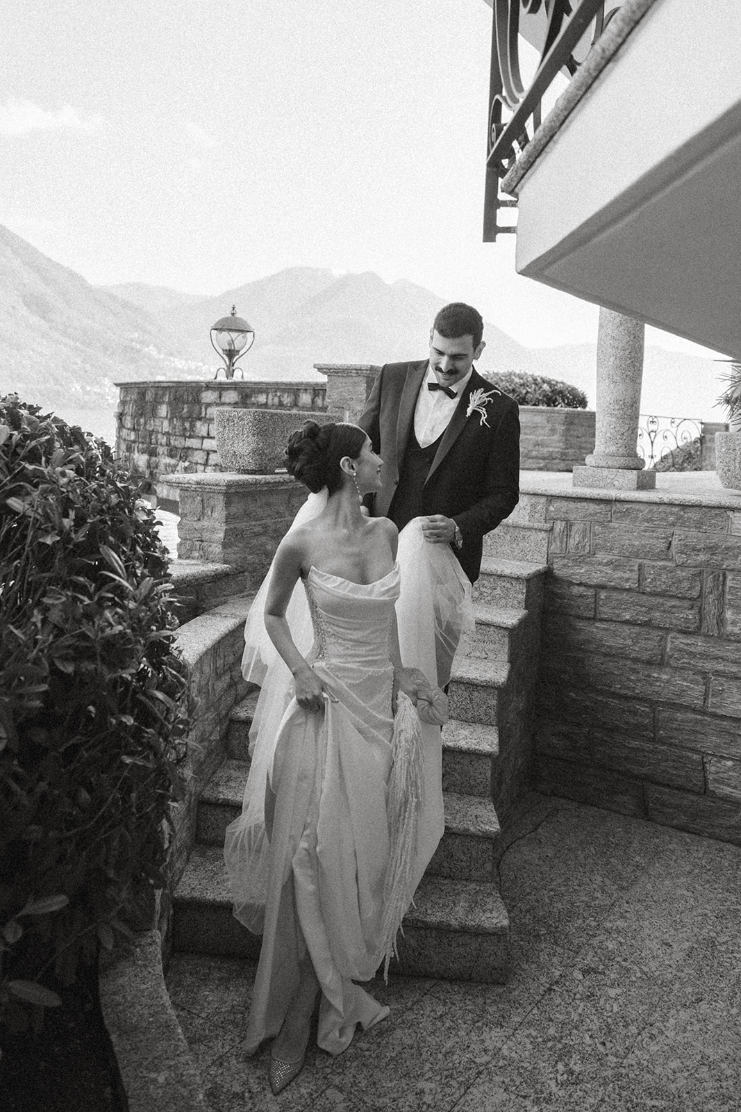 Bride leading the groom down stone steps outside a Lake Como villa, captured in a timeless black-and-white wedding portrait.