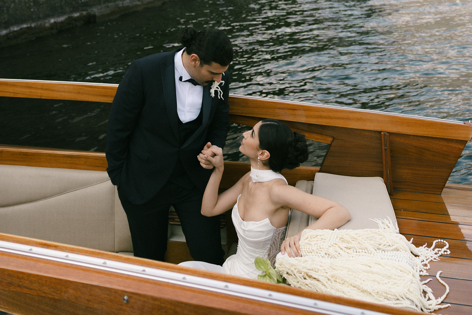 Bride and groom holding hands aboard a classic wooden boat during a Lake Como wedding, surrounded by calm water and elegant floral styling.