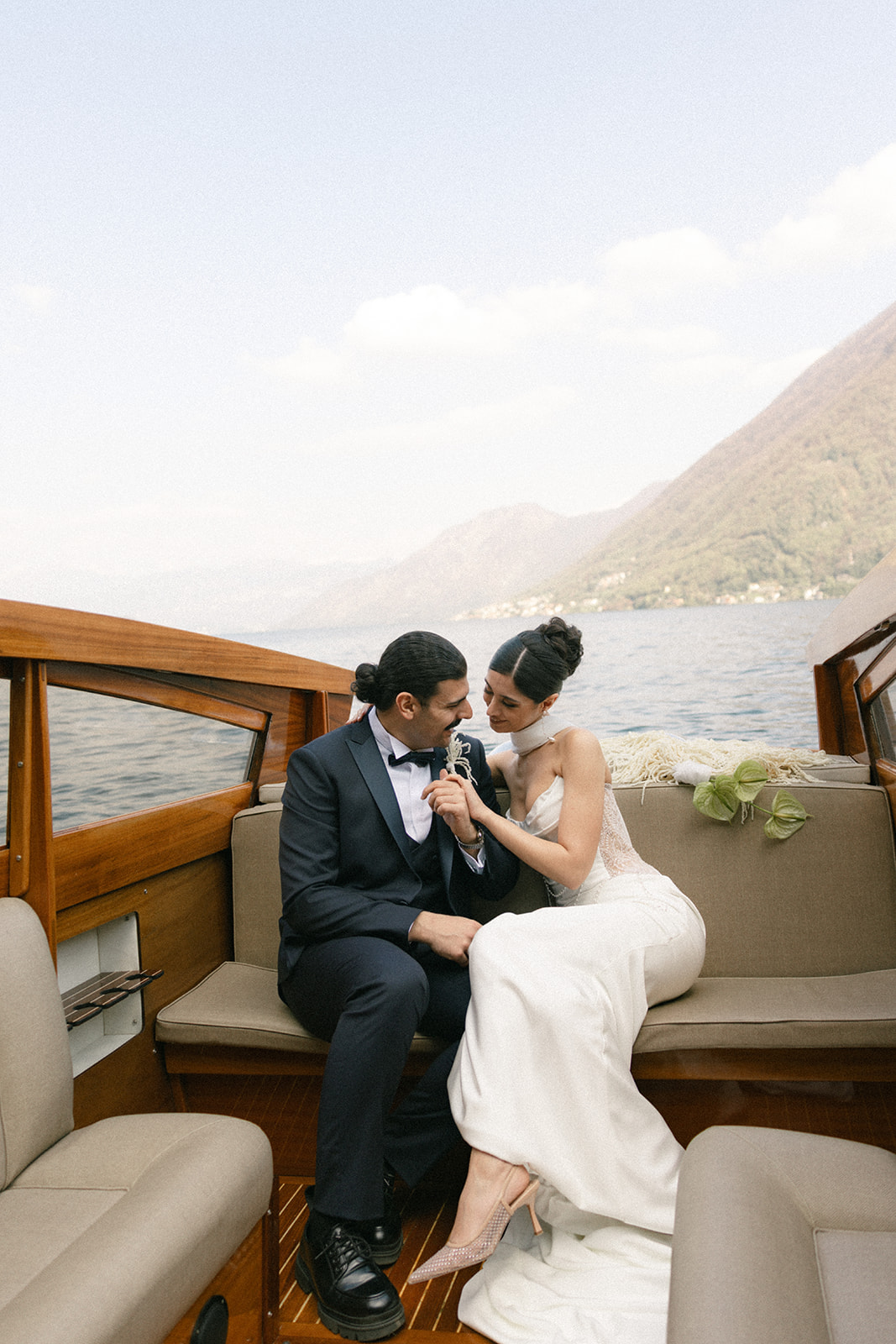 Bride and groom sharing a quiet moment on a vintage wooden boat, photographed by a destination wedding photographer with Lake Como in the background.