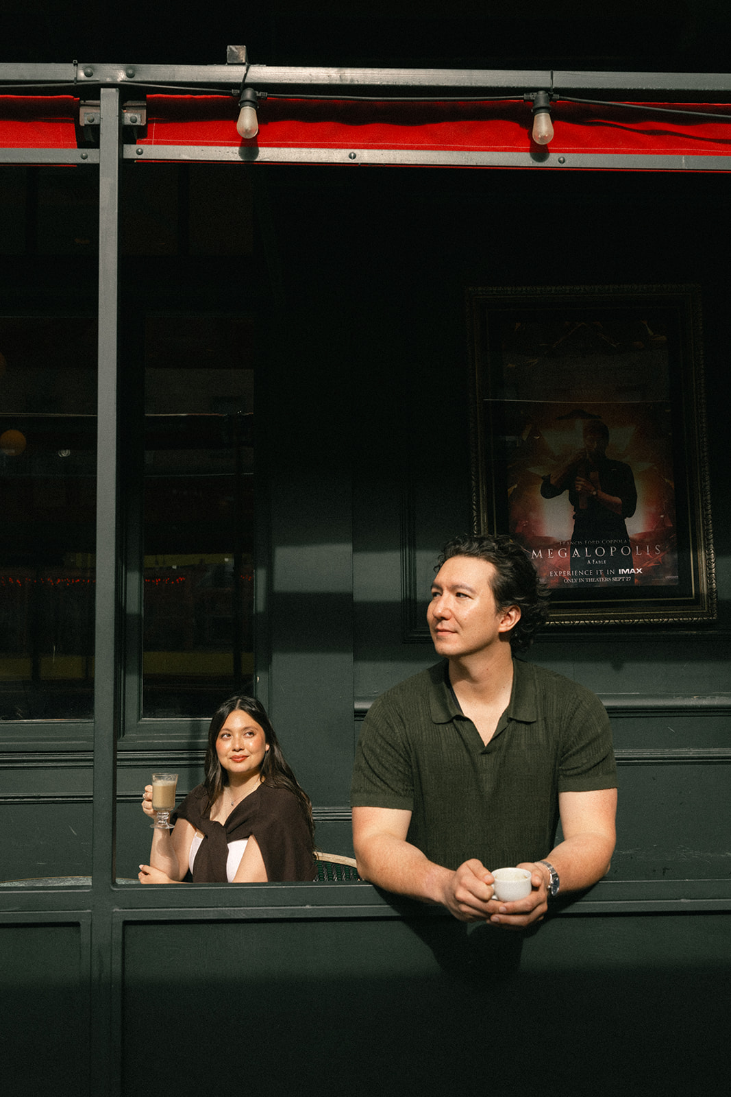 Couple enjoying coffee outside a downtown café, framed by dark storefront windows, warm afternoon light, and classic San Francisco City Streets architecture in the background.