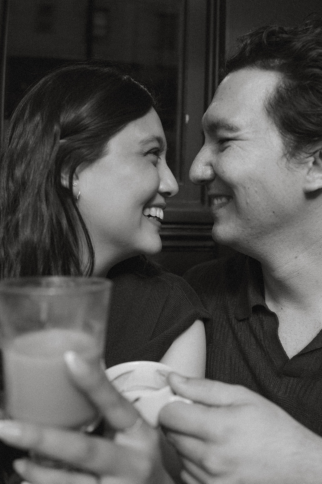 Close-up black and white portrait of a smiling couple sitting together inside a cozy café, making eye contact across the table during an intimate San Francisco engagement photos session captured by a San Francisco photographer.