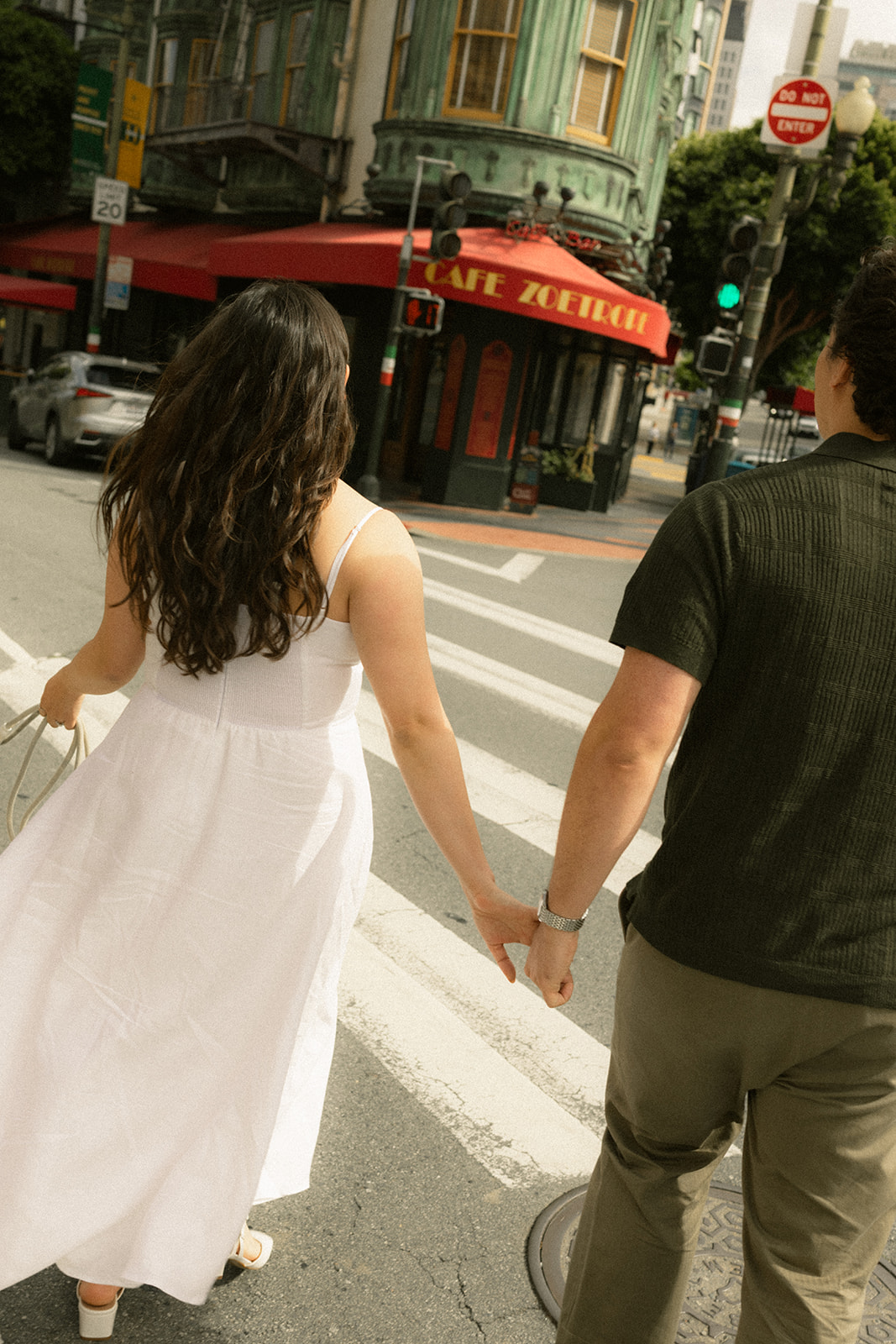 Couple holding hands while crossing a downtown intersection, with Café Zoetrope, crosswalks, and bustling San Francisco City Streets creating an iconic urban backdrop.
