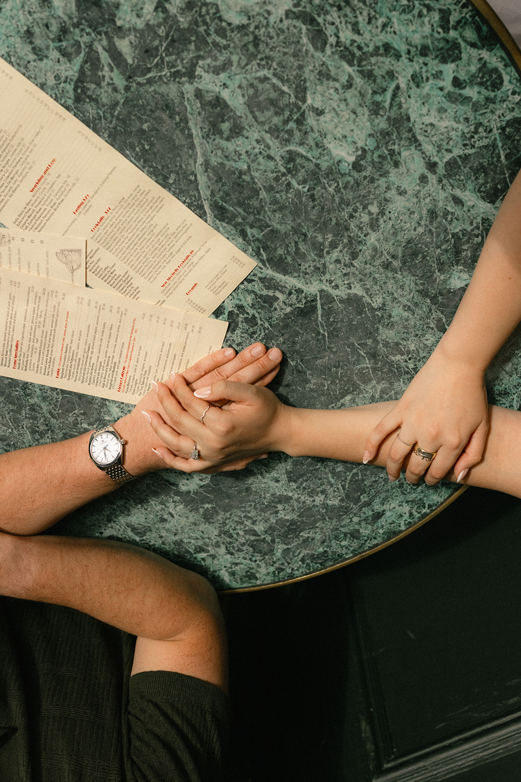 Overhead view of a couple holding hands across a marble café table with coffee menus and drinks, photographed by a San Francisco photographer.