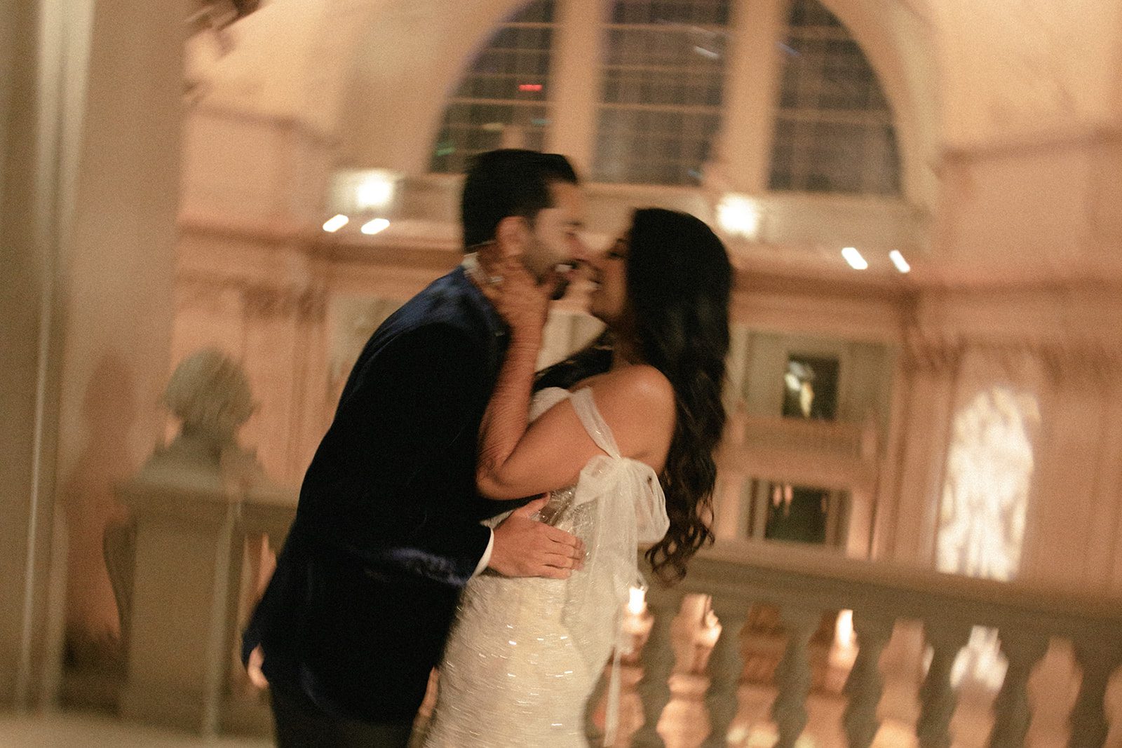 Bride and groom share a kiss inside their San Francisco City Hall wedding, framed by the building’s grand arches and warm evening light.