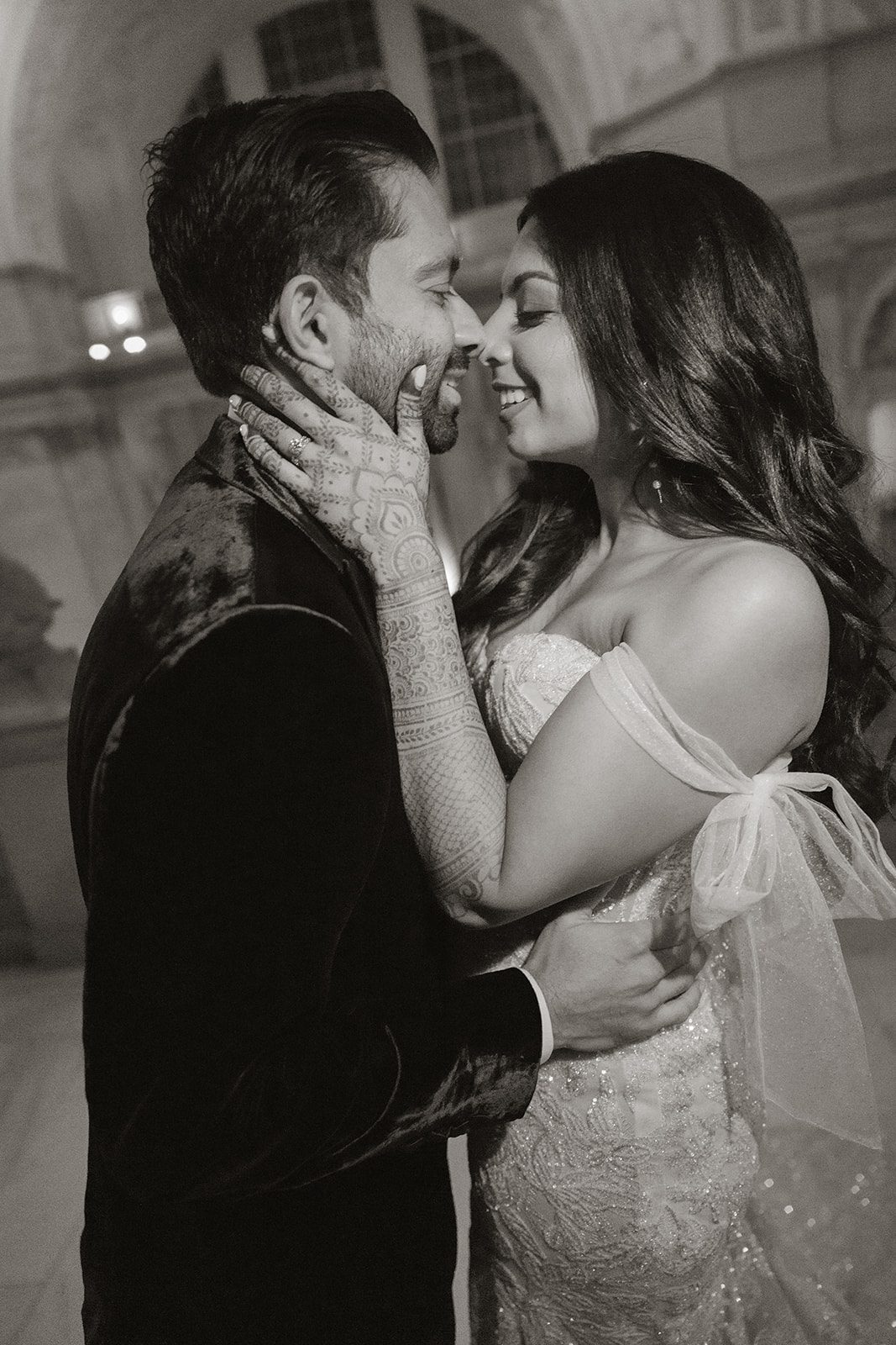 Black-and-white San Francisco City Hall wedding portrait of a couple embracing, with the bride’s detailed henna and off-the-shoulder gown in focus.
