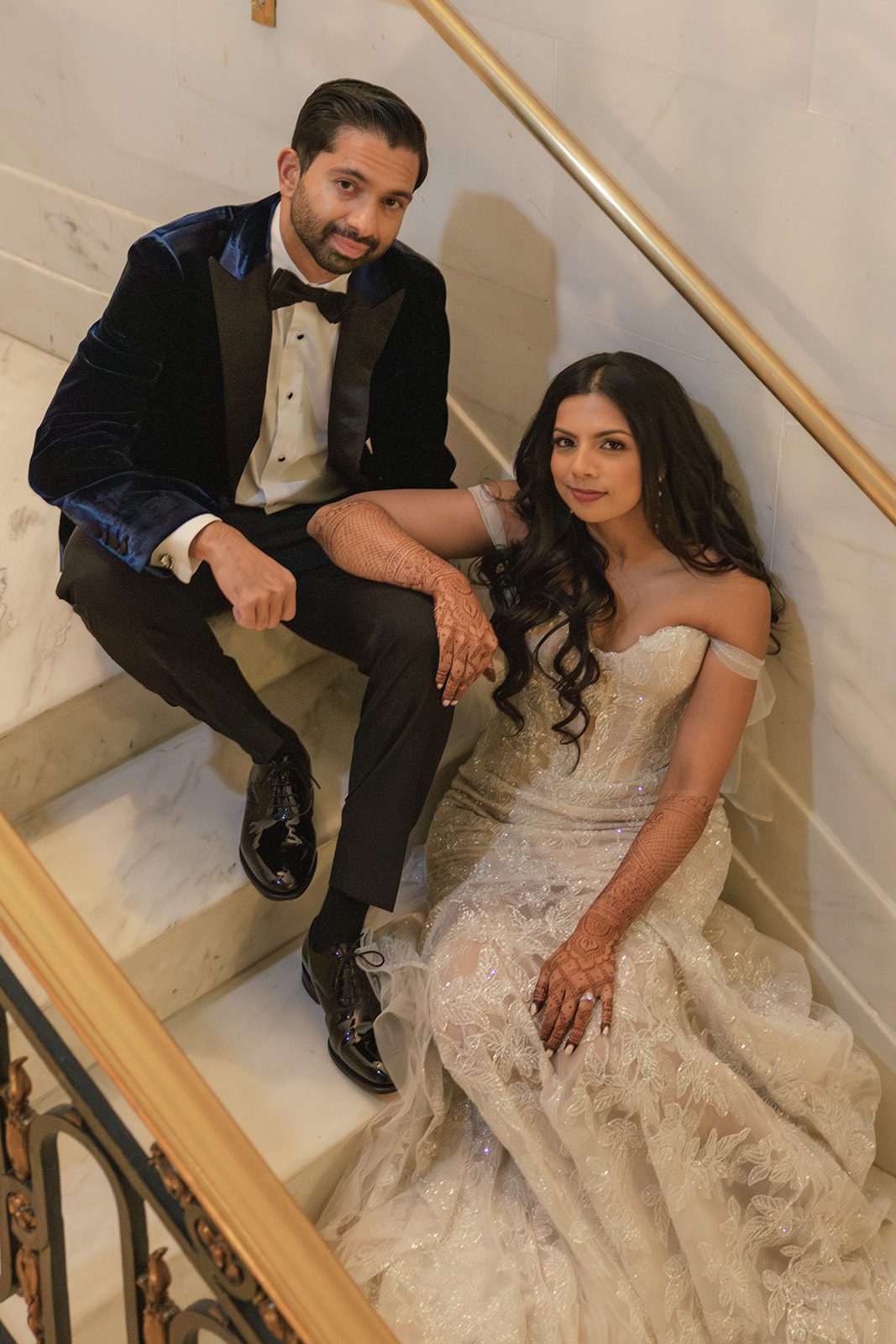 Couple seated together on a marble staircase for a San Francisco City Hall wedding portrait, showcasing the bride’s detailed mehndi and embellished gown.