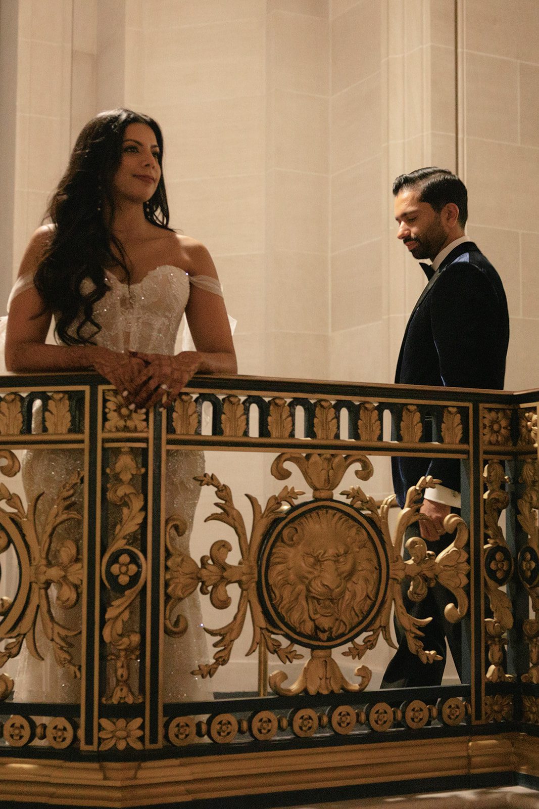Couple standing behind an ornate gold railing inside San Francisco City Hall, with the bride’s detailed mehndi visible.
