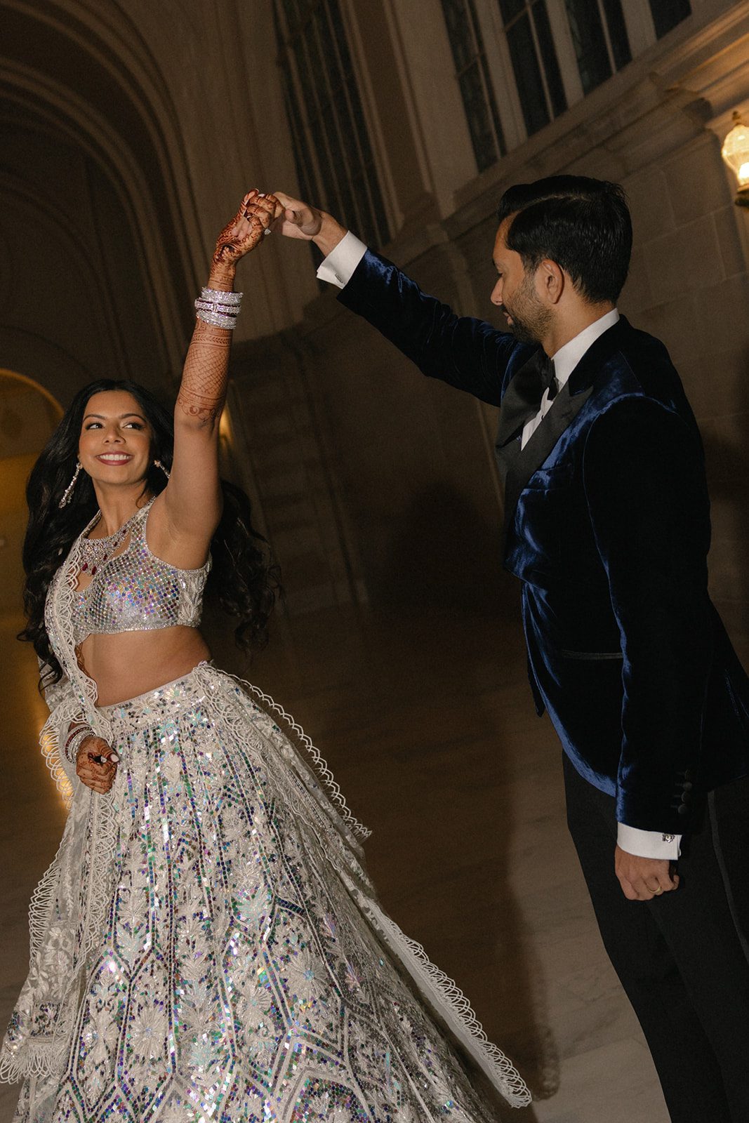 Couple twirling together during a San Francisco City Hall wedding portrait, with the bride wearing a shimmering lehenga and intricate mehndi.