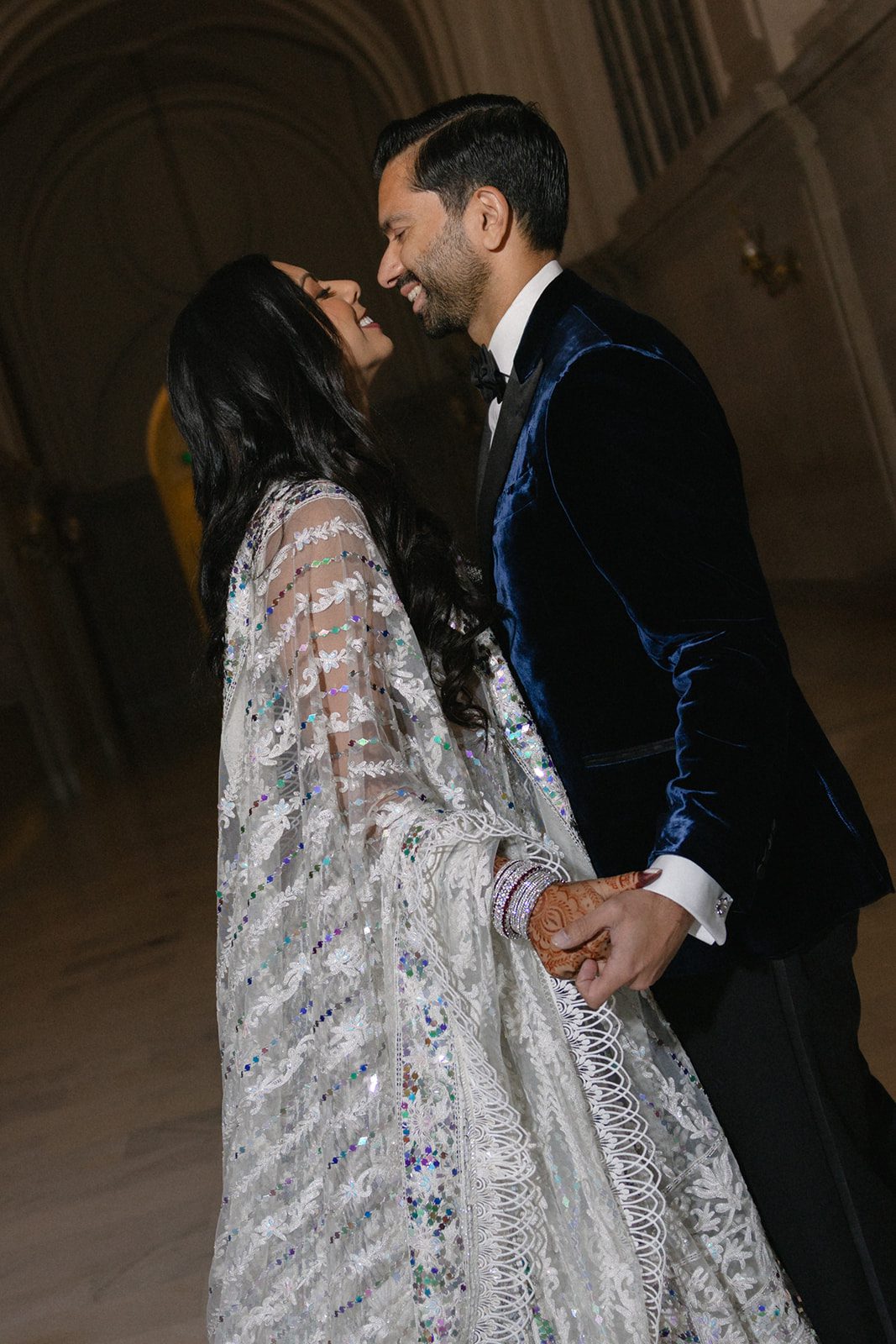 Couple holding hands and smiling during a San Francisco City Hall wedding portrait beneath the building’s arched interior.