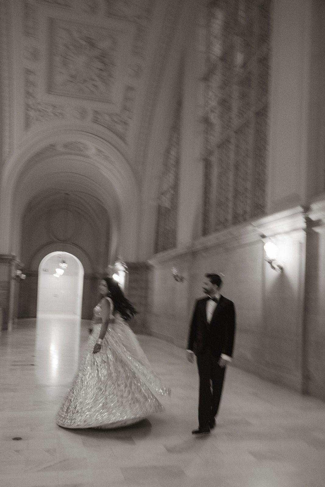 Black-and-white San Francisco City Hall wedding photos of the bride and groom facing each other in an ornate hallway, photographed with intentional motion blur.