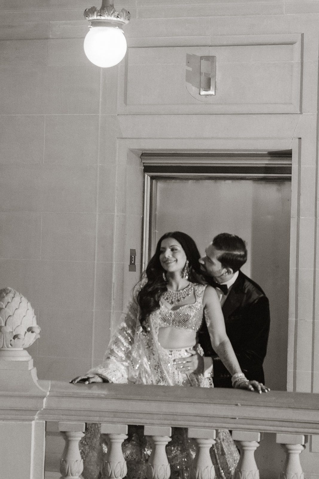 Black-and-white portrait of newlyweds embracing on a City Hall balcony, captured by a San Francisco City Hall photographer against the building’s classic stone architecture.