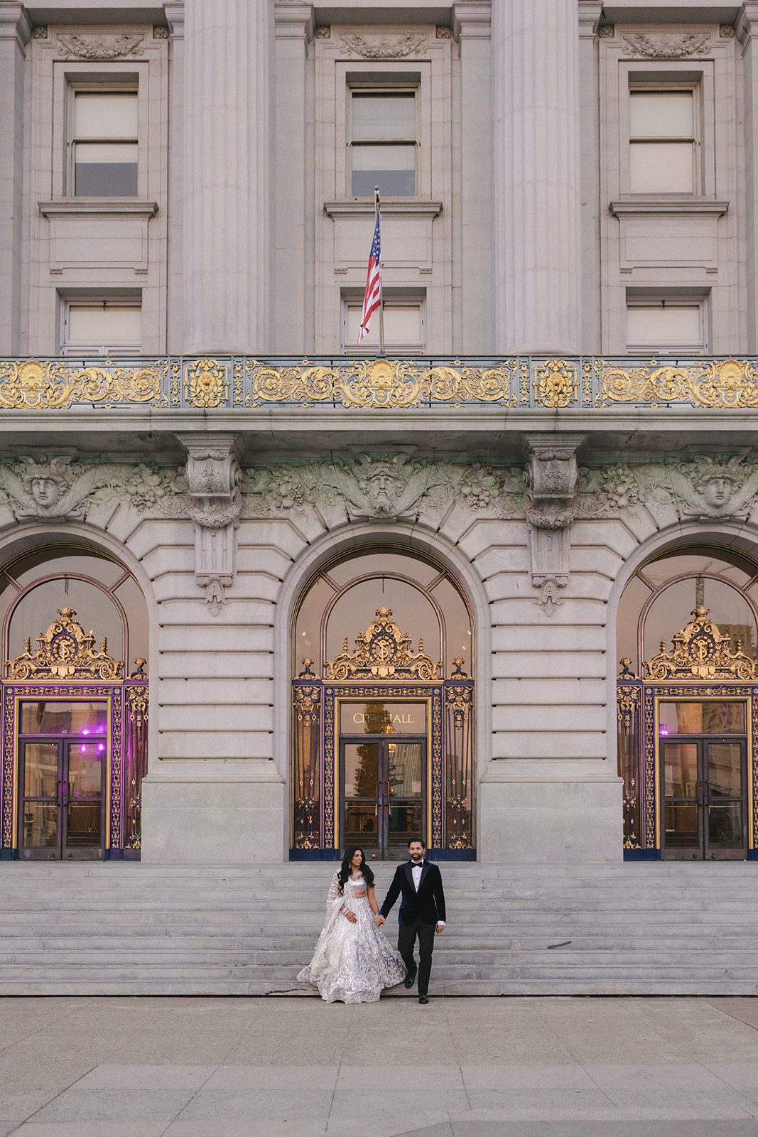 Couple walking down the front steps beneath the ornate entrance of their San Francisco City Hall wedding venue.