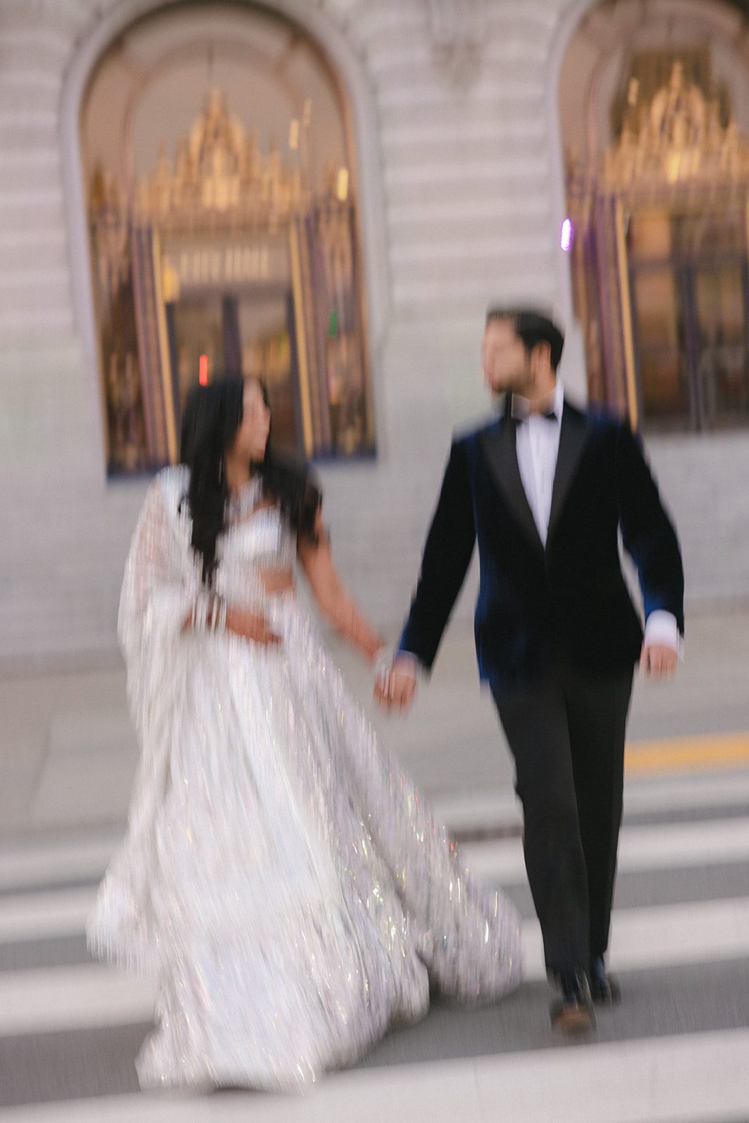 Motion-blurred couple holding hands while crossing the street during their San Francisco City Hall wedding.