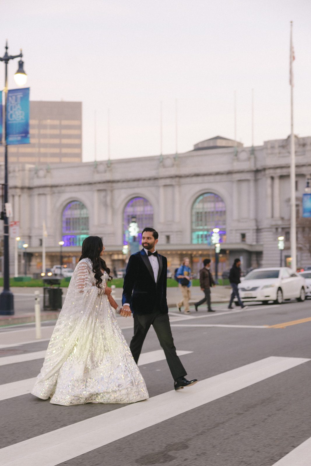 Couple walking hand in hand across a crosswalk near San Francisco City Hall after their wedding.