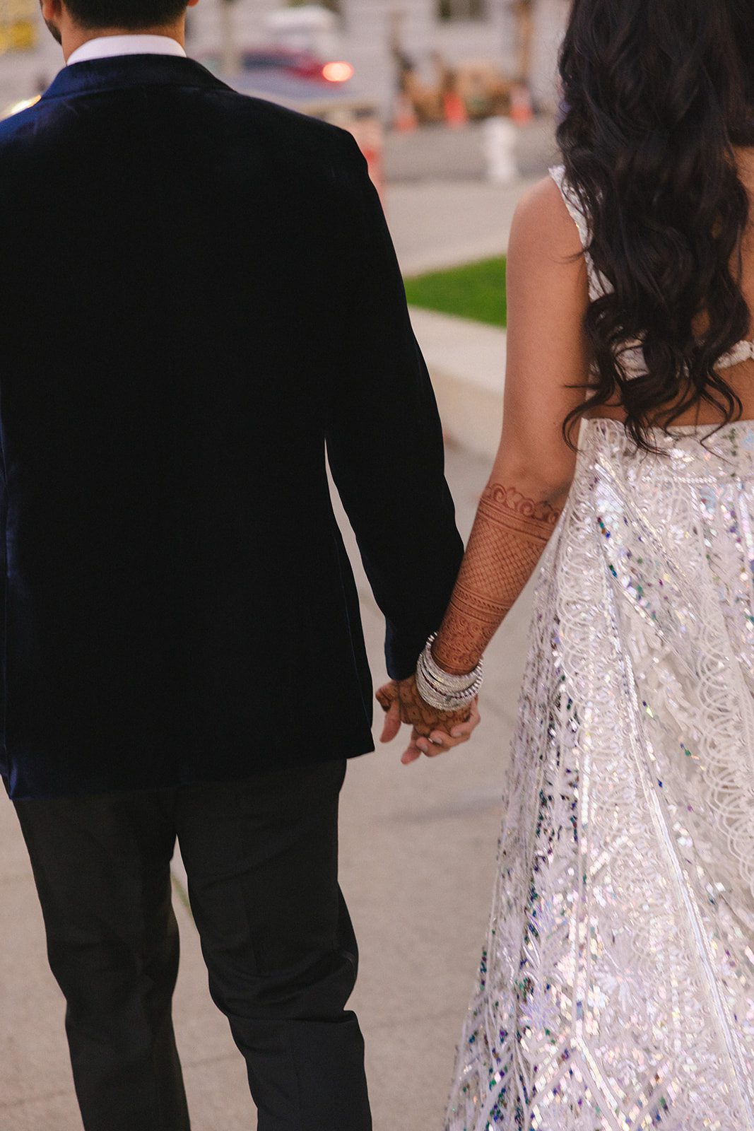 Close-up San Francisco City Hall wedding photos of the couple walking hand in hand, highlighting the bride’s intricate henna, silver bangles, and embellished lehenga.
