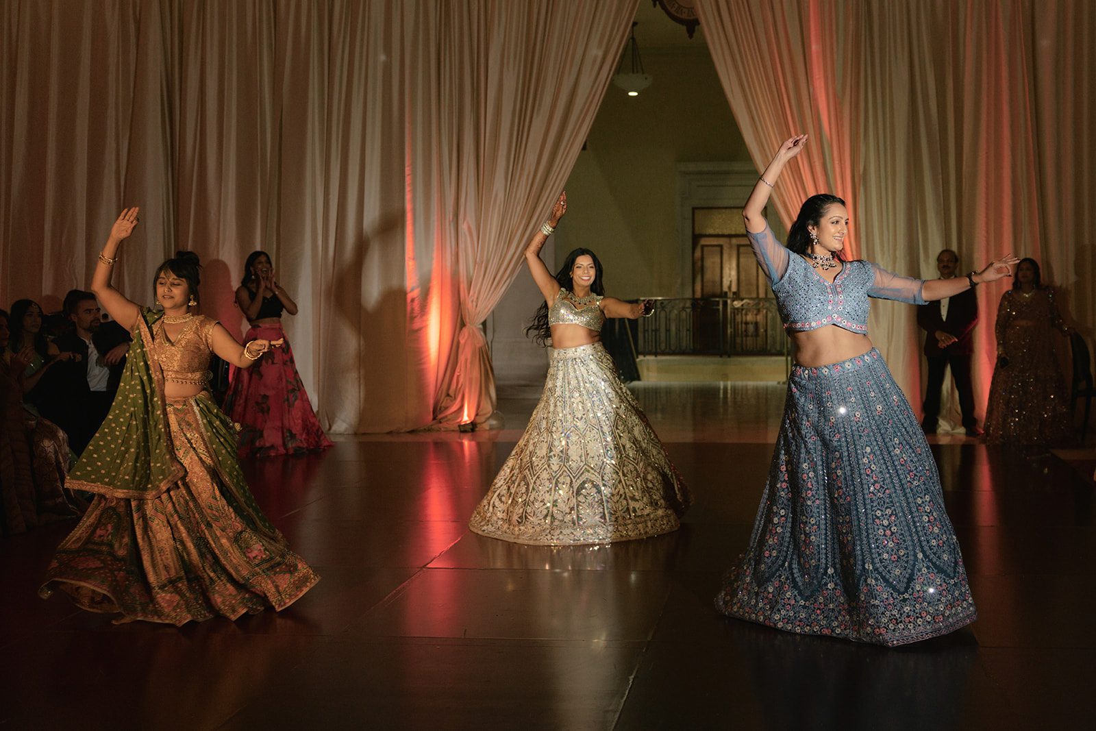 Guests perform a choreographed dance in colorful lehengas during the San Francisco City Hall wedding reception, framed by draped curtains and warm uplighting.