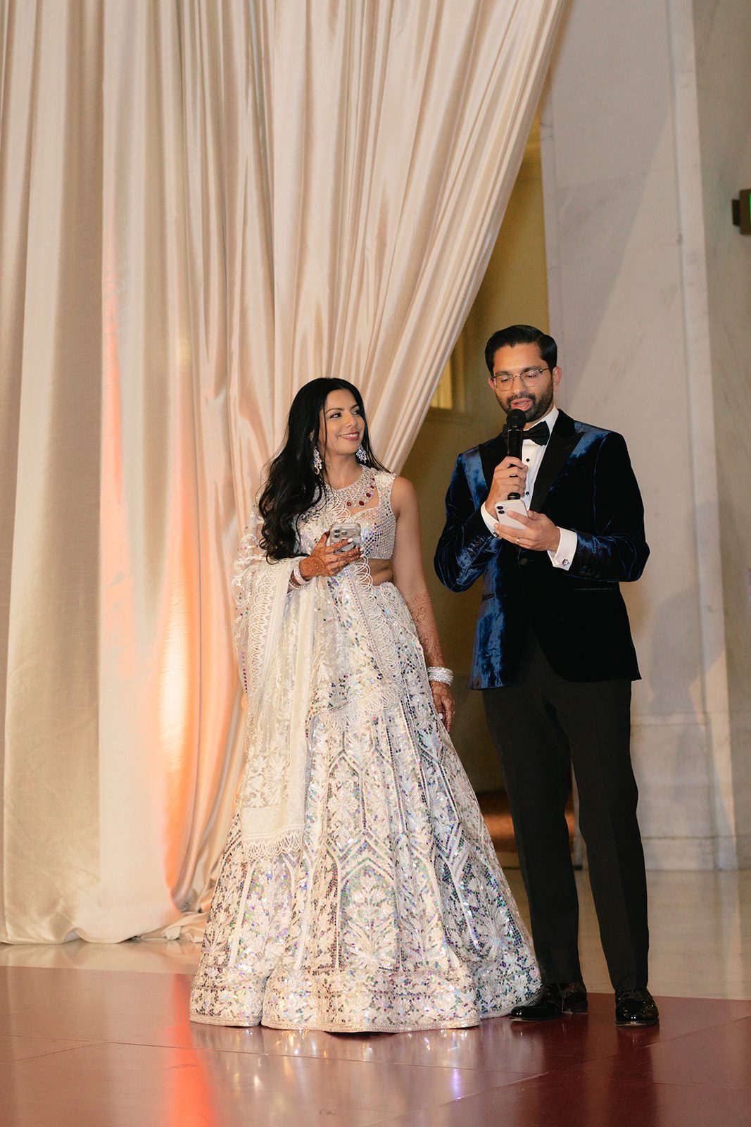 Groom gives a speech beside the bride during their San Francisco City Hall wedding reception, surrounded by elegant draping and warm evening light.