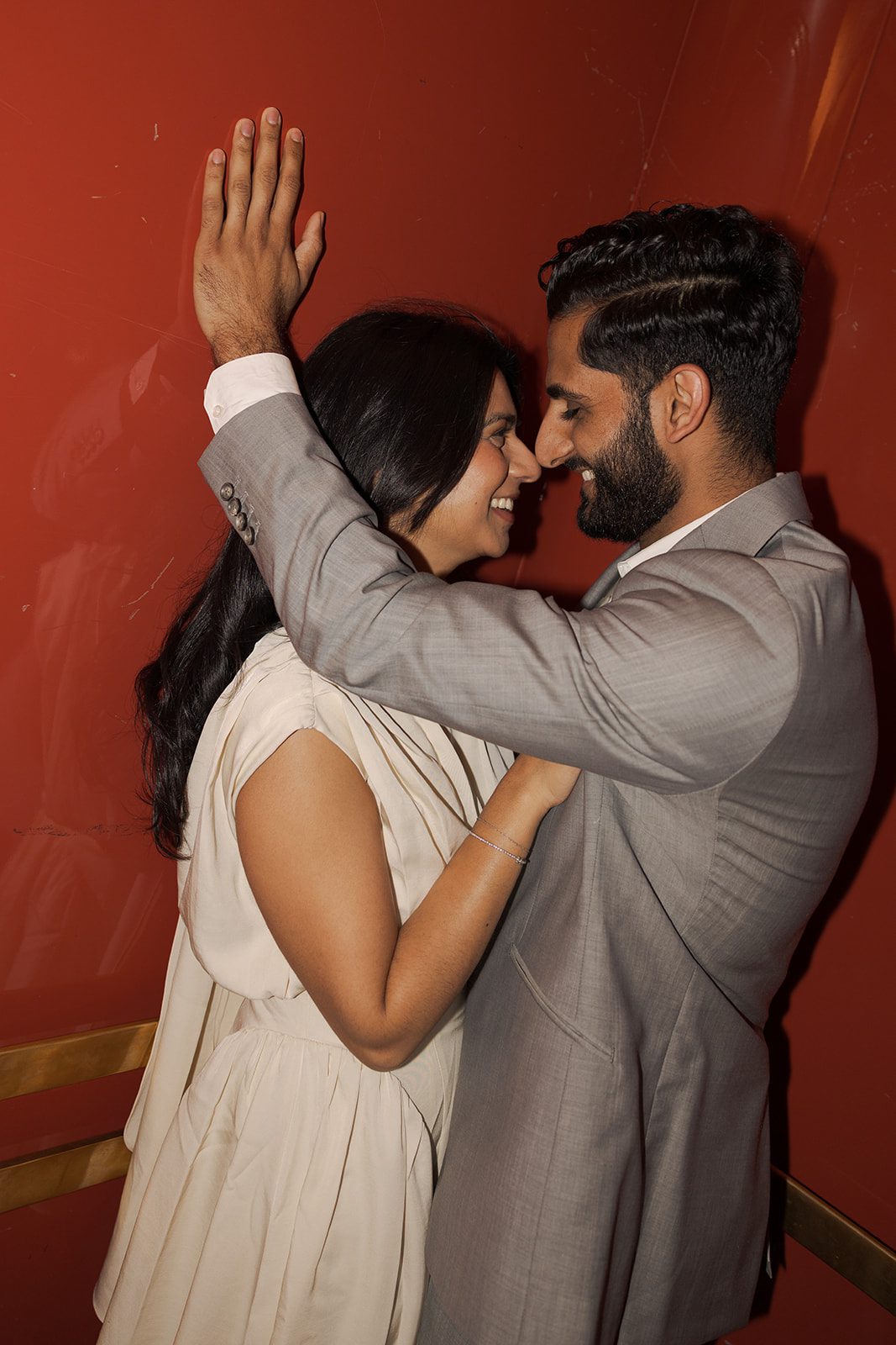 Close-up portrait of a couple smiling face-to-face against a deep red interior wall during their Marin County Civic CenterElopement, captured with direct flash by a Bay Area wedding photographer.