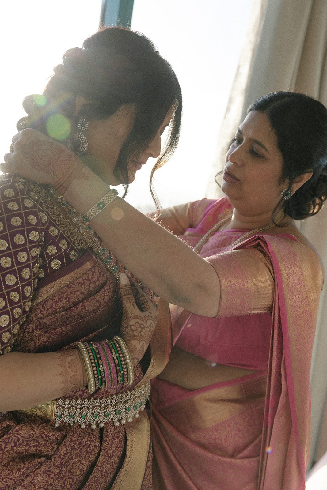 Bride’s family member adjusts her jewelry and sari while she gets ready for her multi-day wedding celebration in San Francisco.