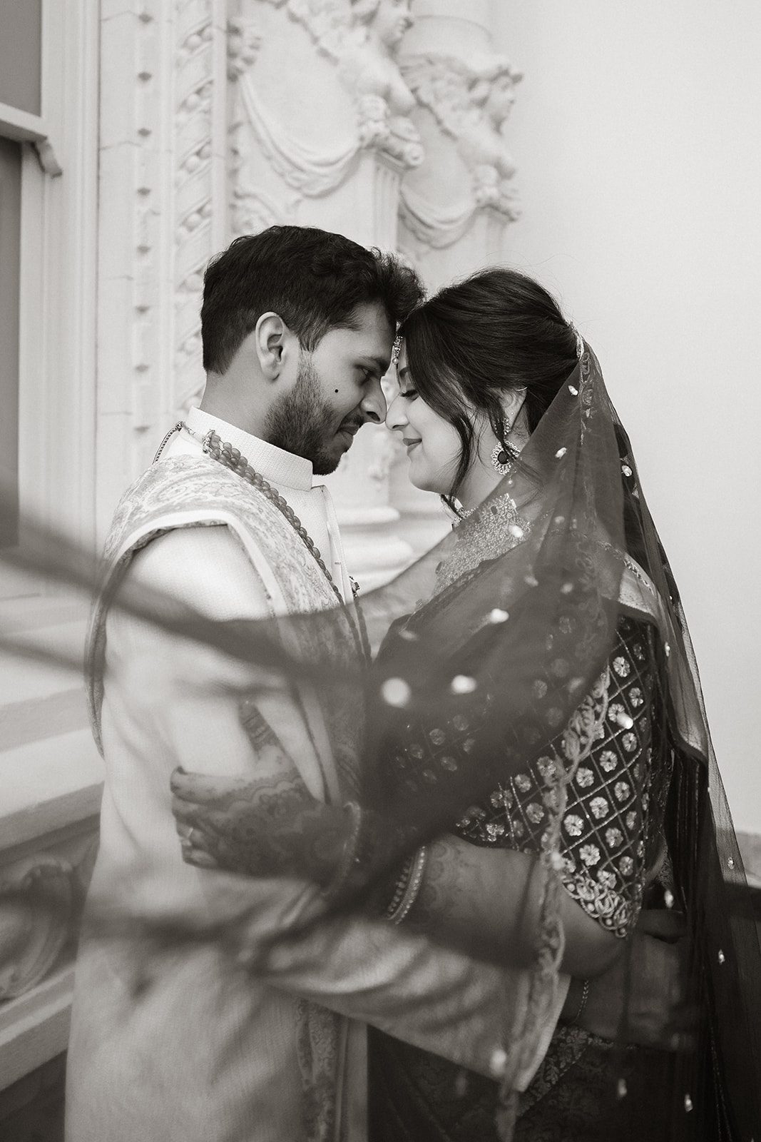Black-and-white portrait of an Indian wedding couple embracing beneath the ornate architecture of the Conservatory at One Sansome.