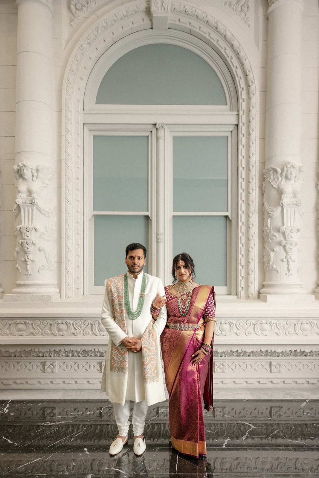 Indian wedding couple in traditional attire framed by the ornate white architecture of the Conservatory at One Sansome.