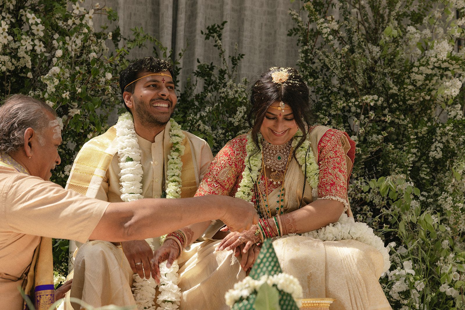 Bride and groom smiling during a traditional Telugu wedding ceremony surrounded by white florals at the Conservatory at One Sansome.