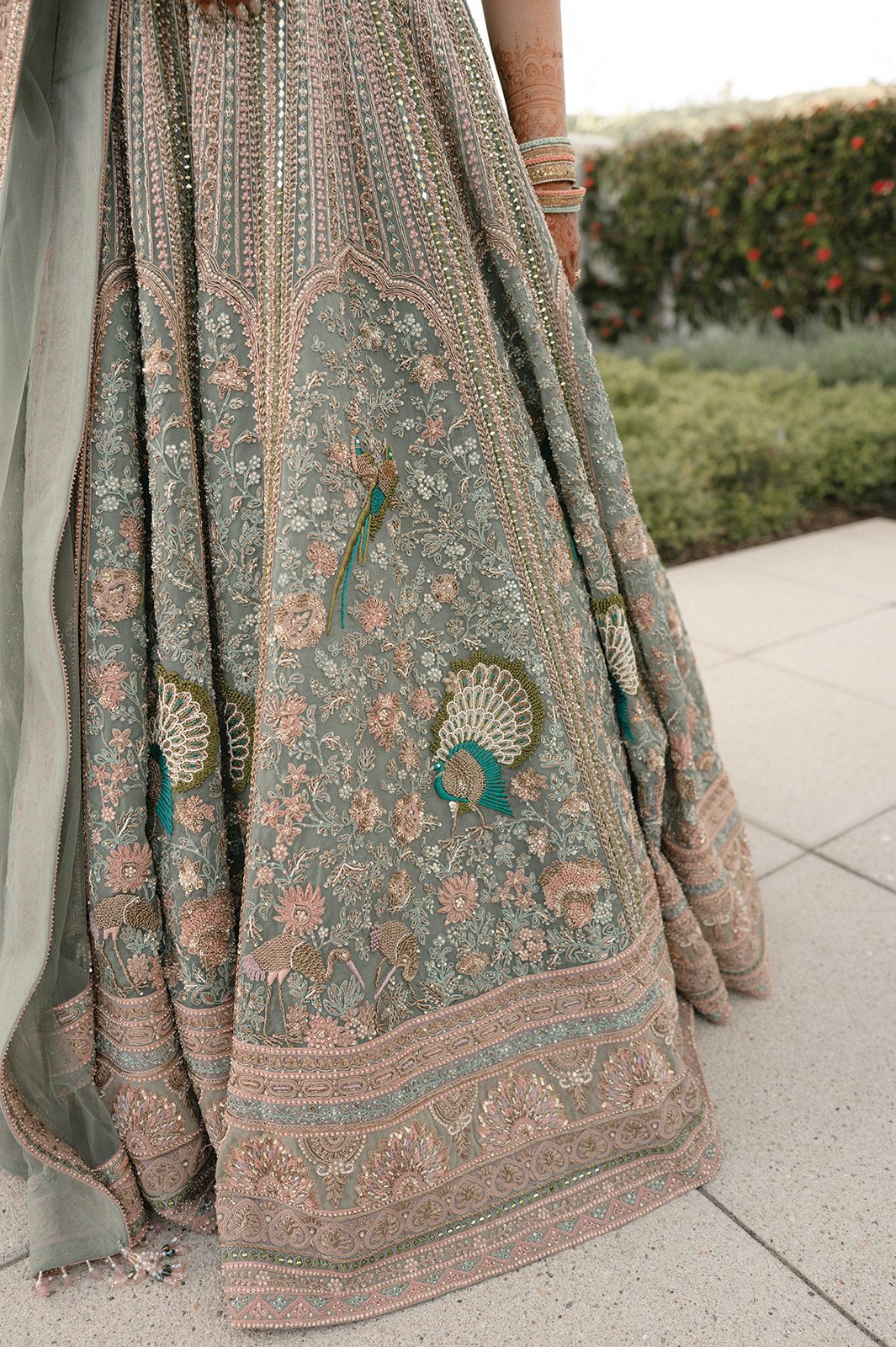 Close-up of intricate peacock embroidery and beadwork on the bride’s sage green lehenga during the multi-day wedding.