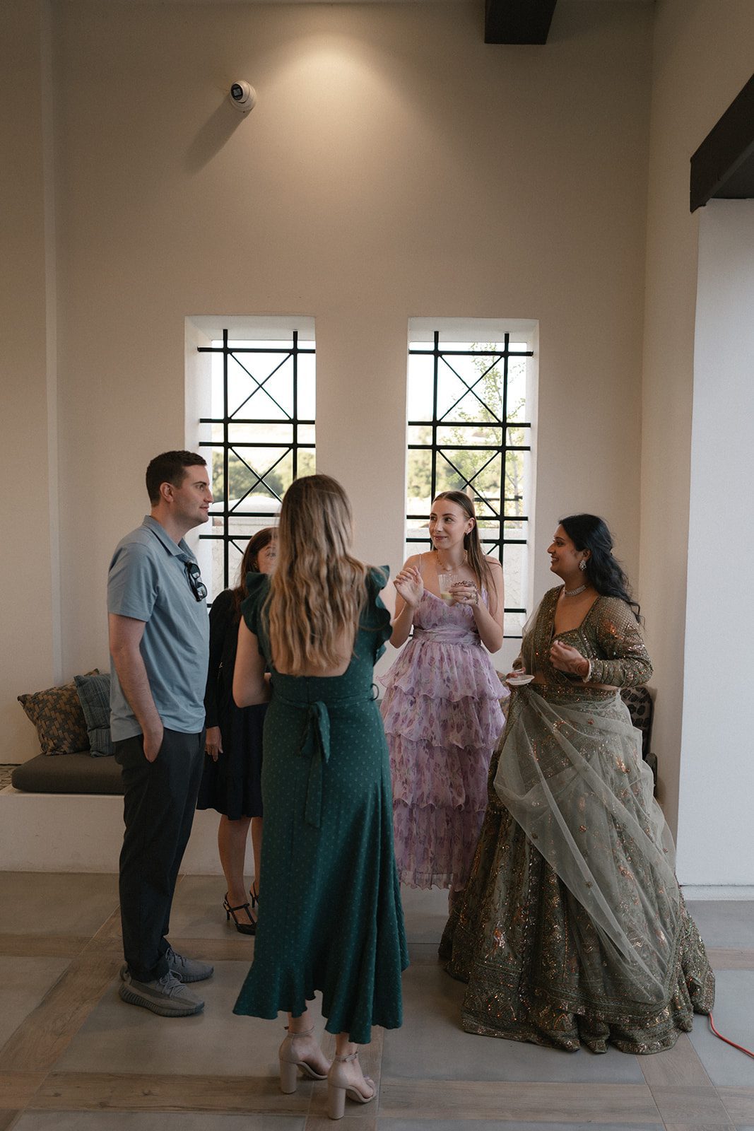 Wedding guests mingle indoors in colorful formal attire during an Indian wedding event.