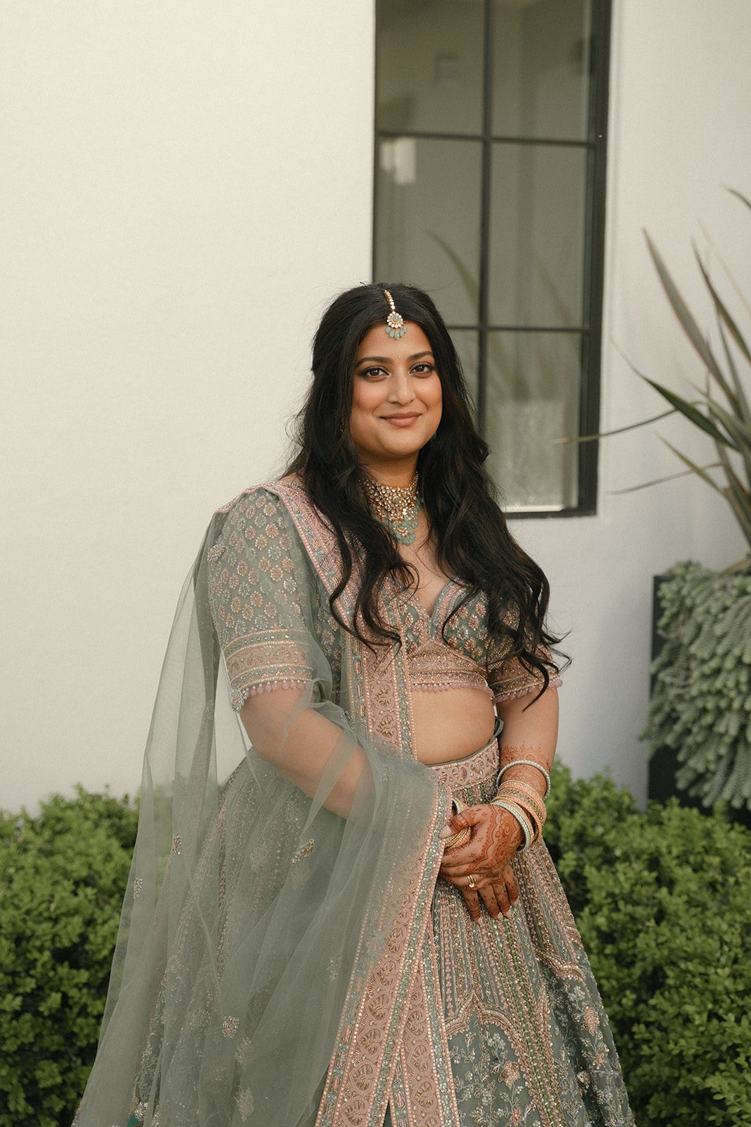 Portrait of the bride in a sage green lehenga with traditional jewelry and mehndi at an Indian wedding.