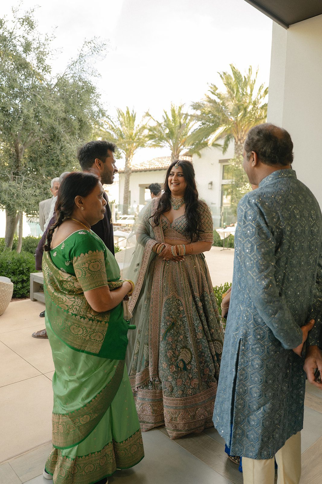 Bride speaking with wedding guests in colorful traditional attire during an outdoor Indian wedding gathering.