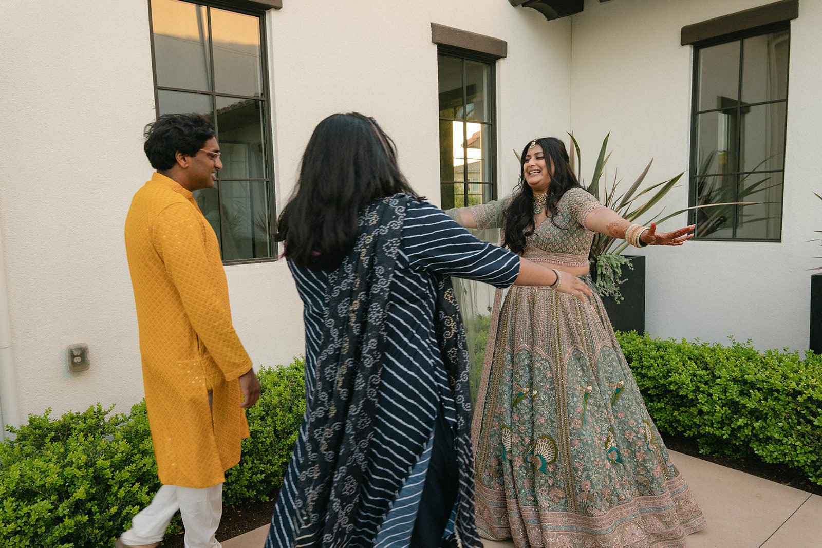 Bride greeting family members outdoors while wearing a sage green embroidered lehenga during an Indian wedding celebration.